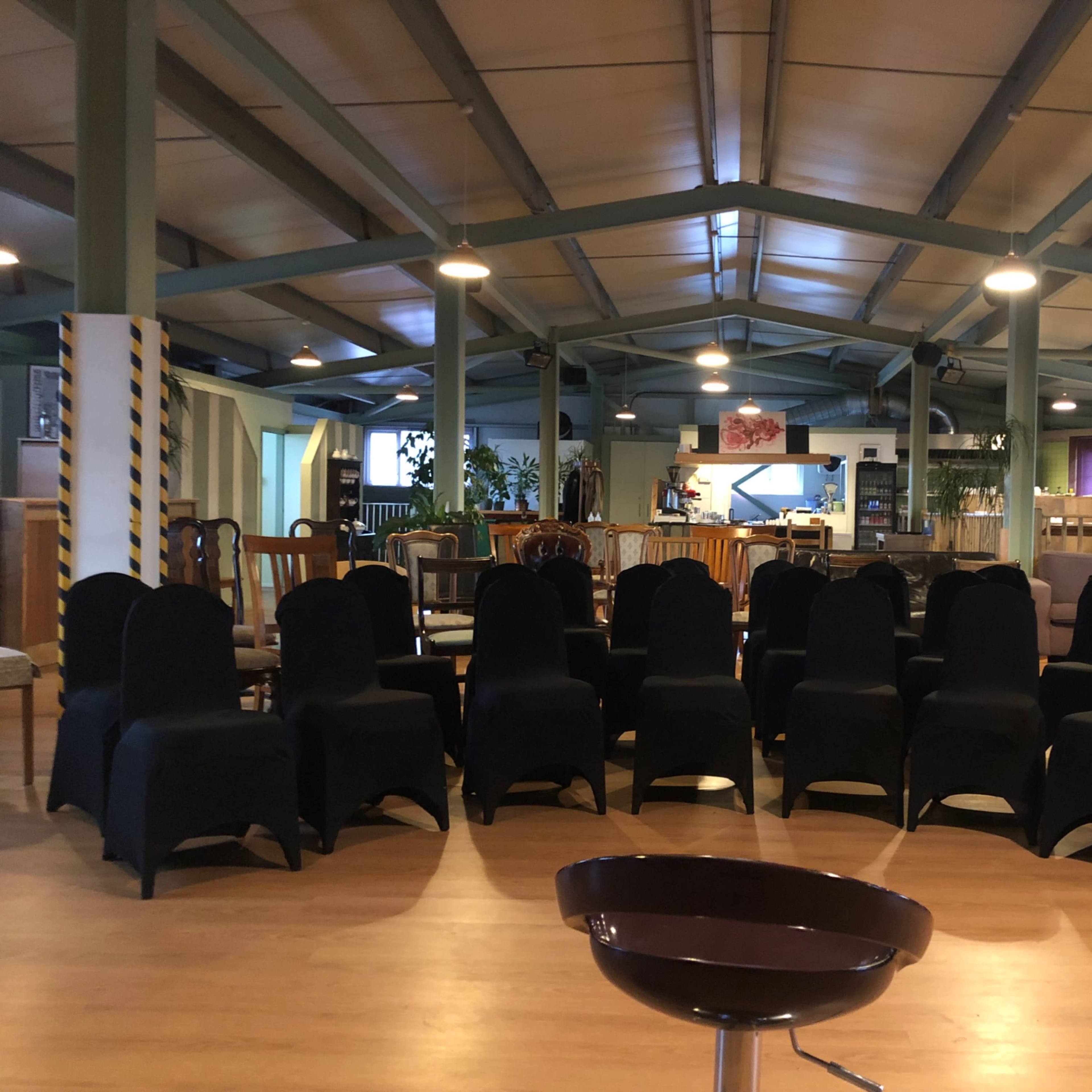 A rows of chairs covered in black fabric arranged in a seating area of a spacious room with high ceilings and wooden flooring.