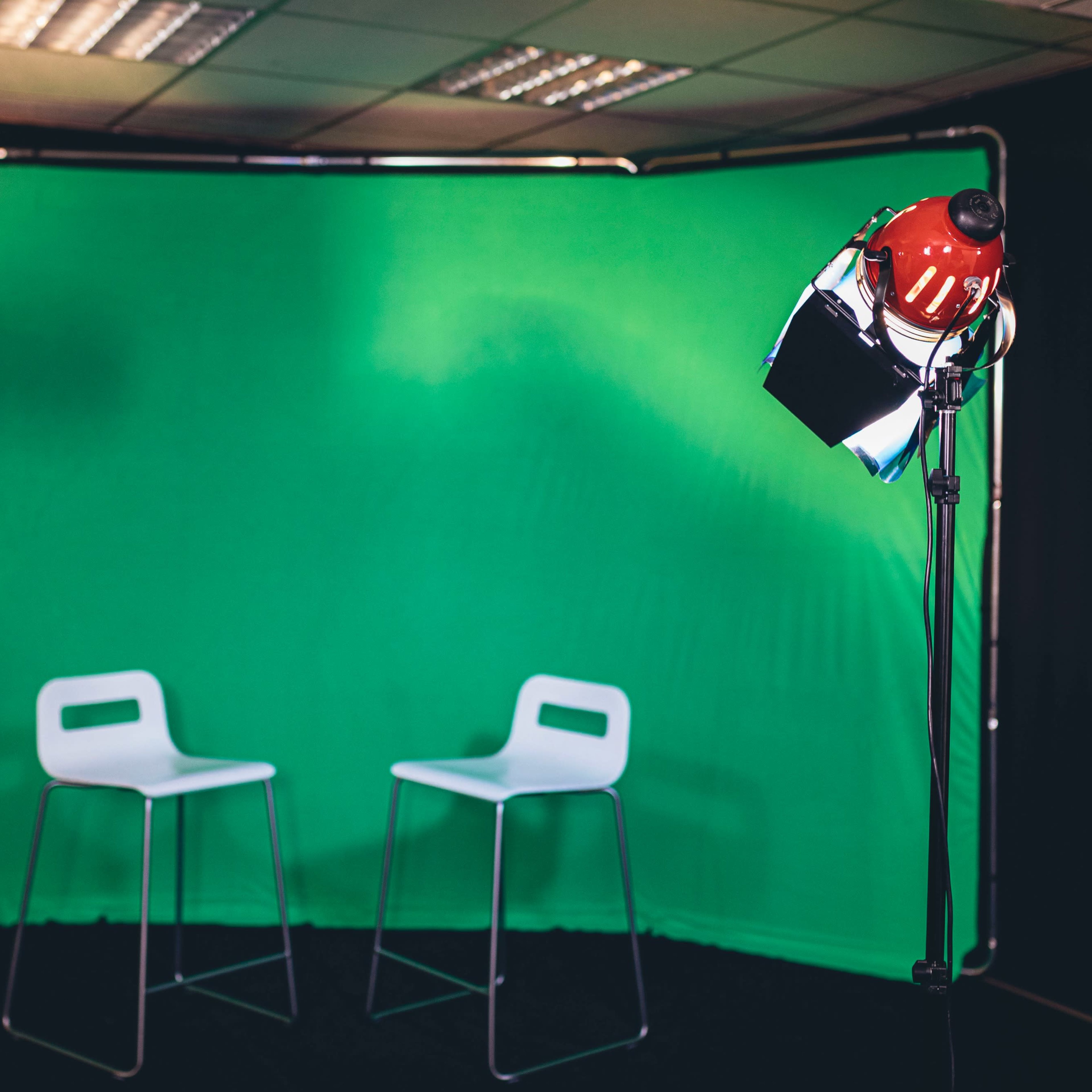 Two white chairs positioned in front of a green backdrop, illuminated by two lighting fixtures on stands.