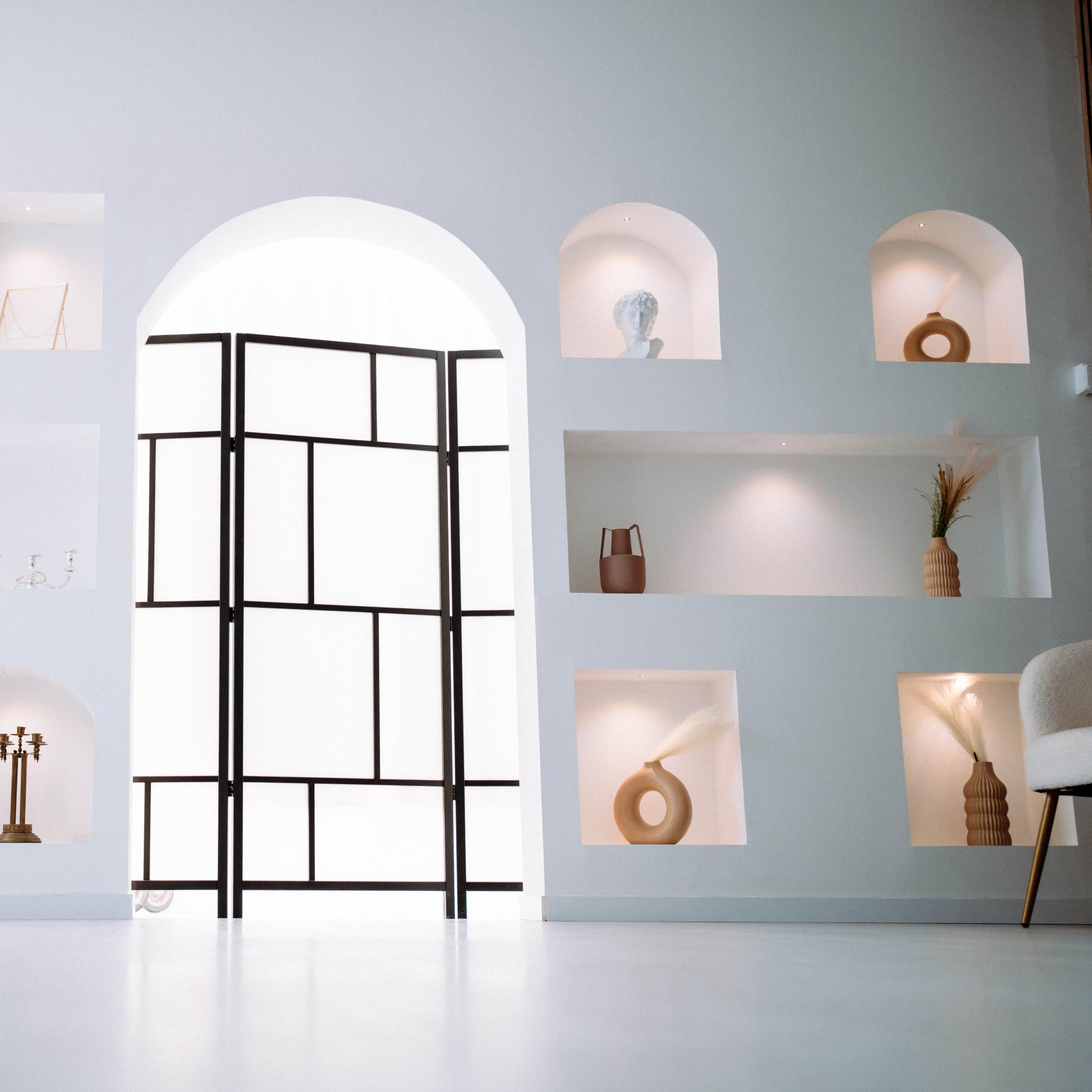 A minimalist room features a black open frame door with a white archway, surrounded by built-in shelves displaying decorative objects.
