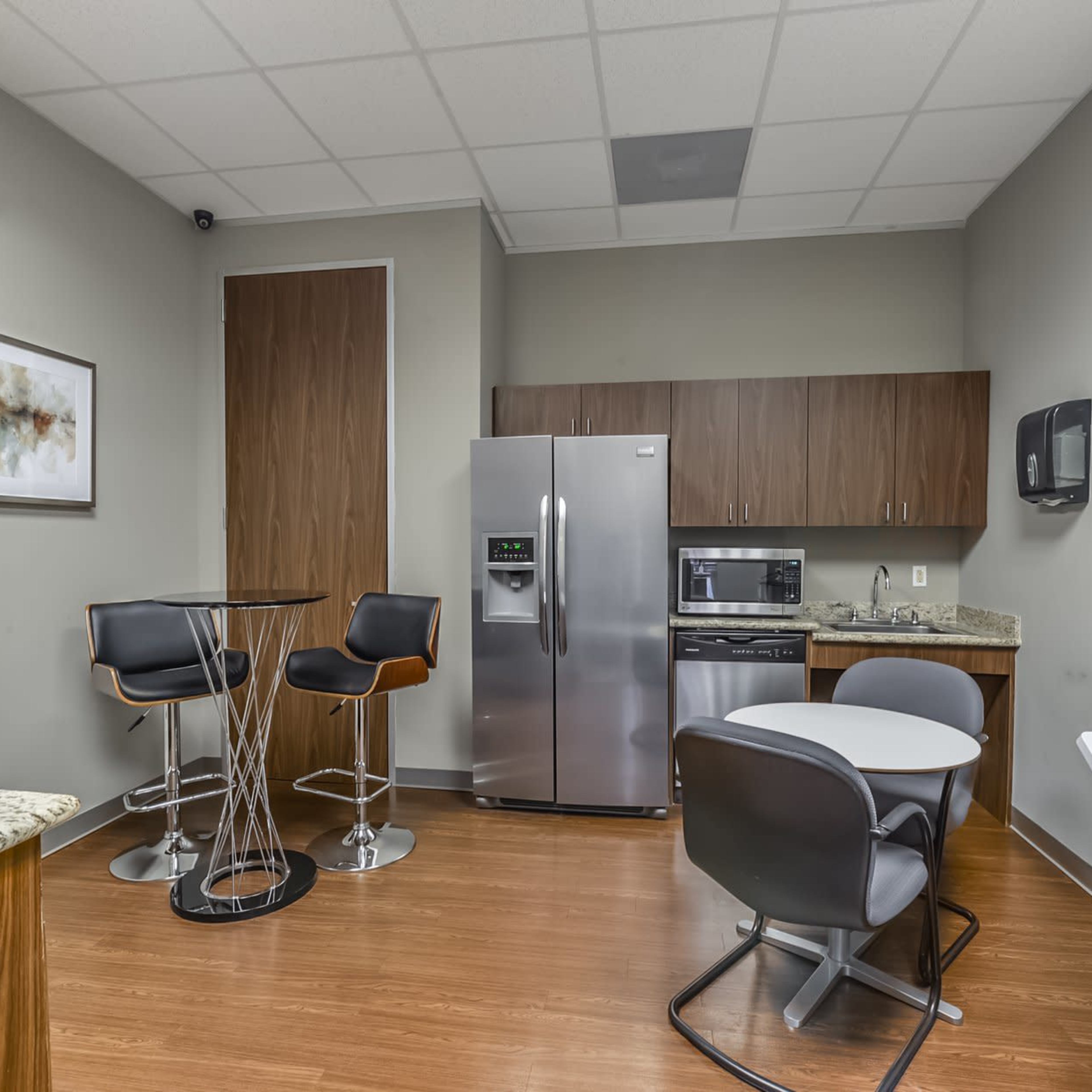A modern conference room features a large wooden table surrounded by black leather chairs, with a television mounted on the wall and glass partitions.