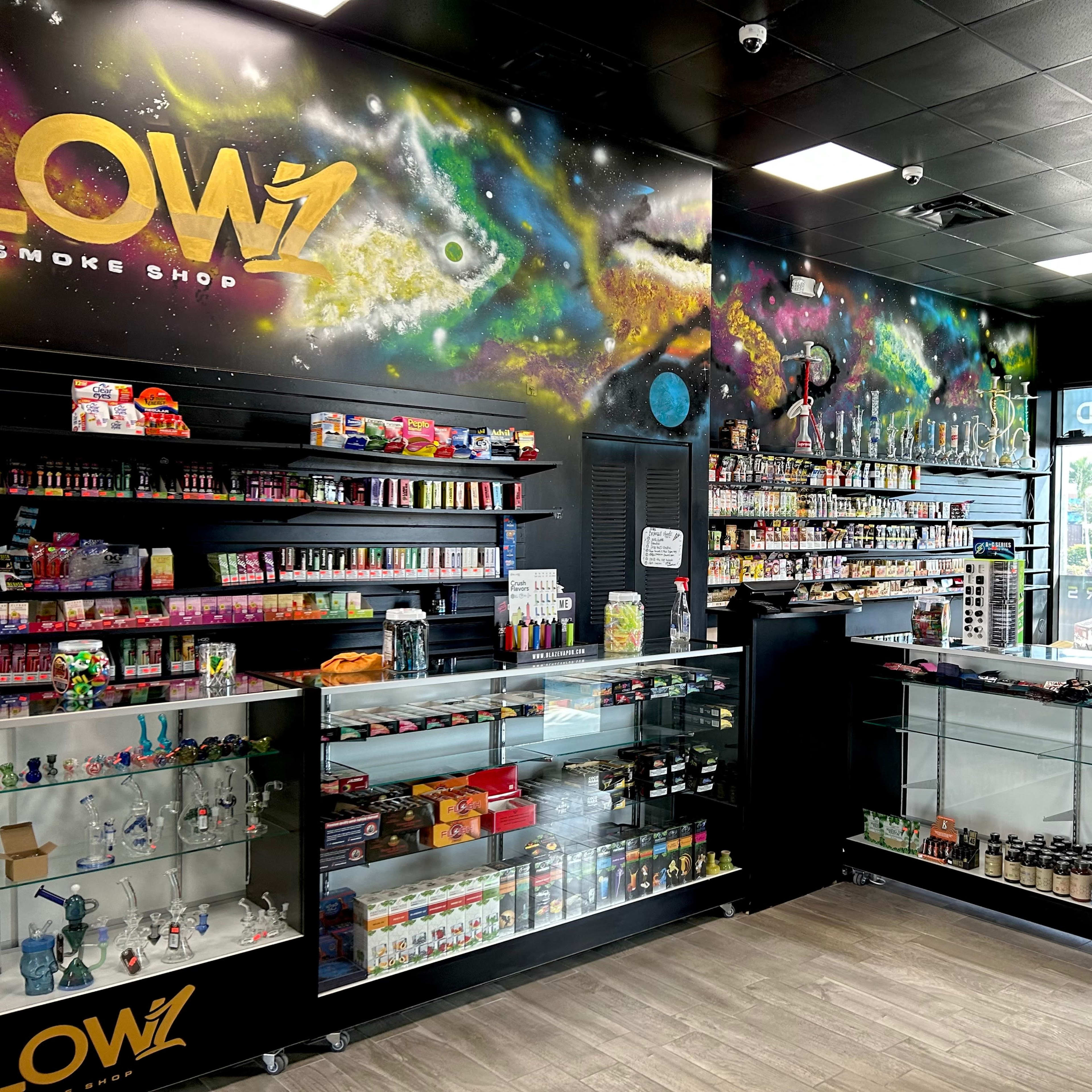 The interior of a smoke shop featuring colorful displays of smoking accessories and products on glass shelves against a mural of a galaxy.