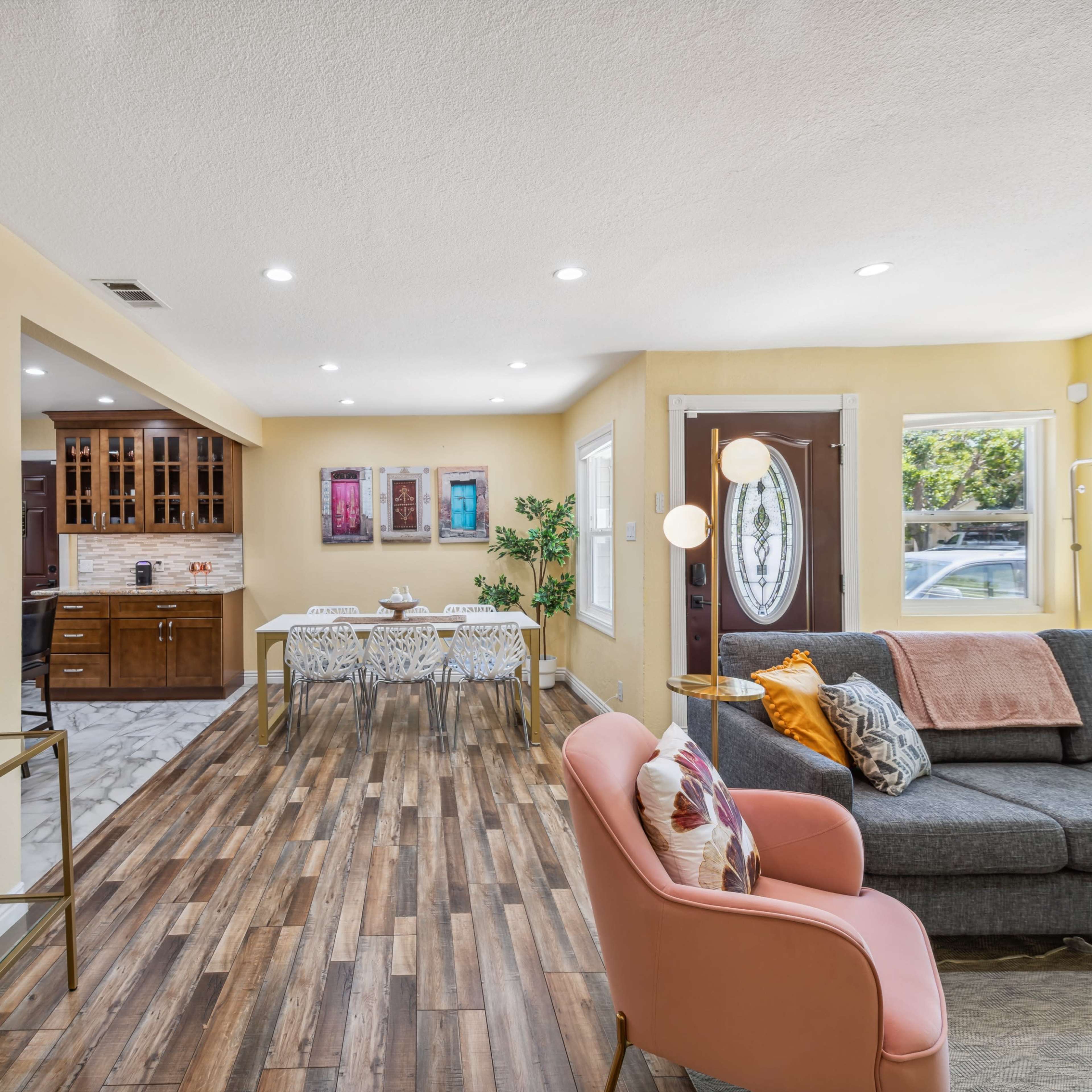 A modern living room with a gray sofa, a pink chair, a dining area with a table, and a kitchen in an open-concept layout.