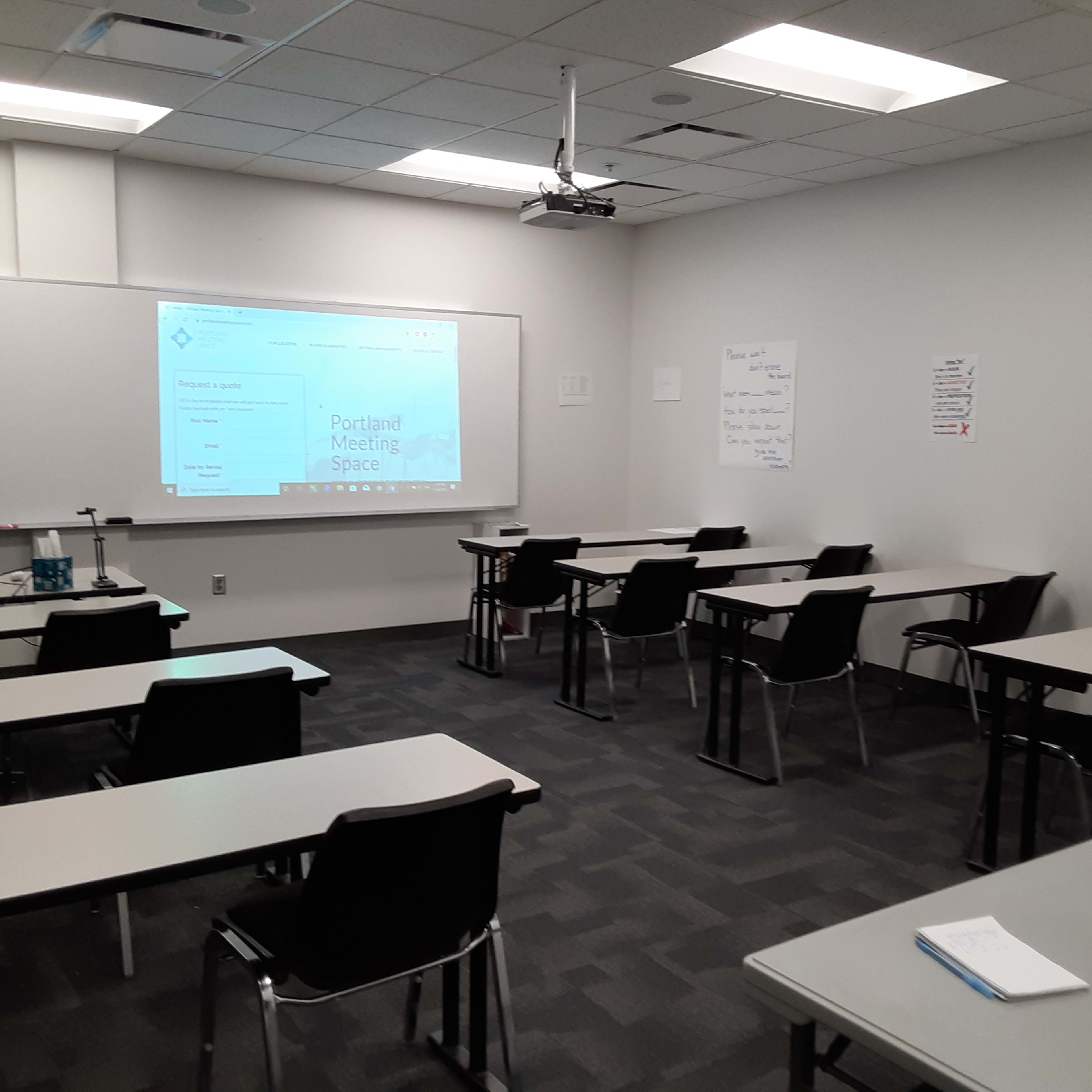 A conference room is configured with rows of tables and chairs, featuring a projector screen displaying a meeting agenda.