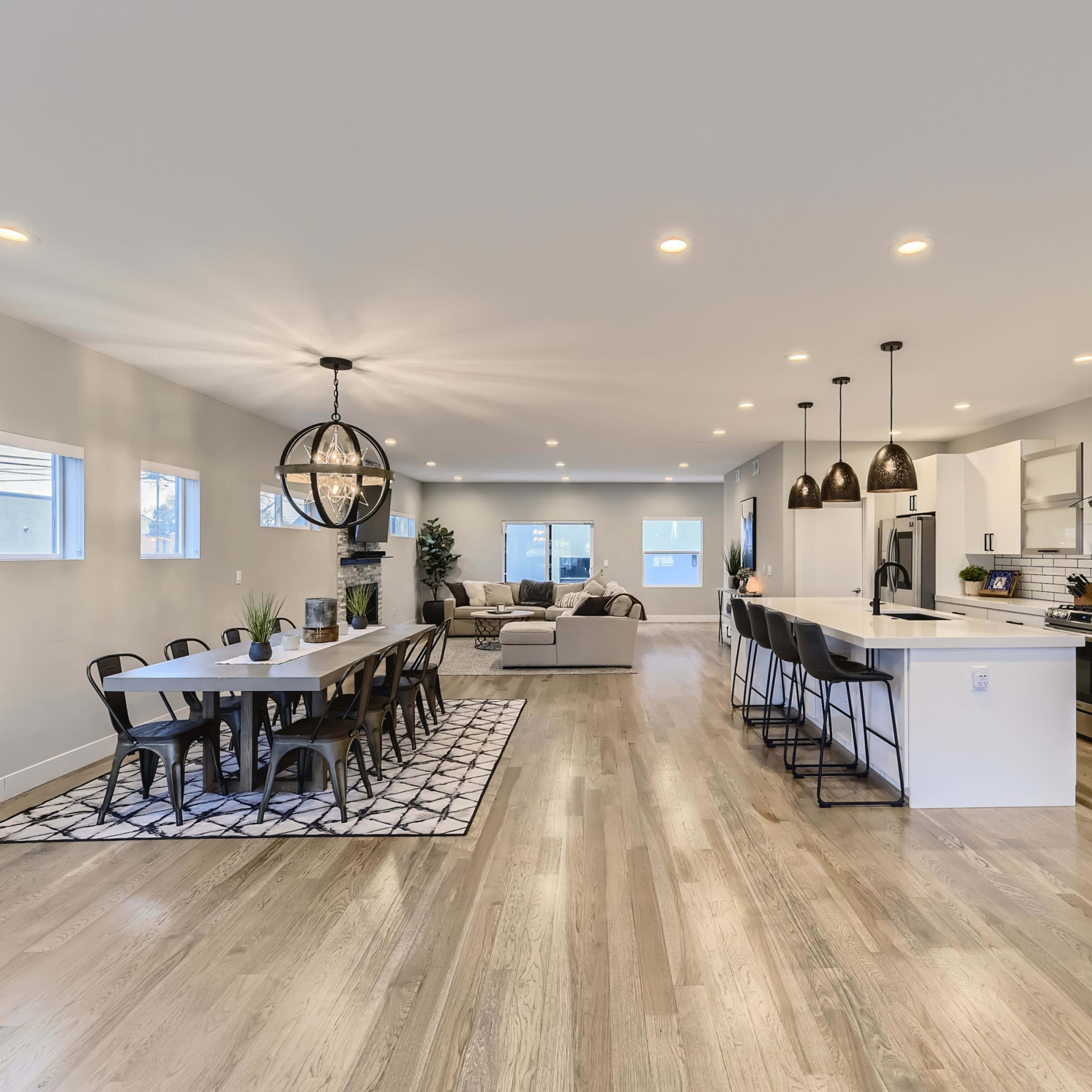 A spacious modern kitchen and dining area with a long table, black chairs, and a living room in the background.