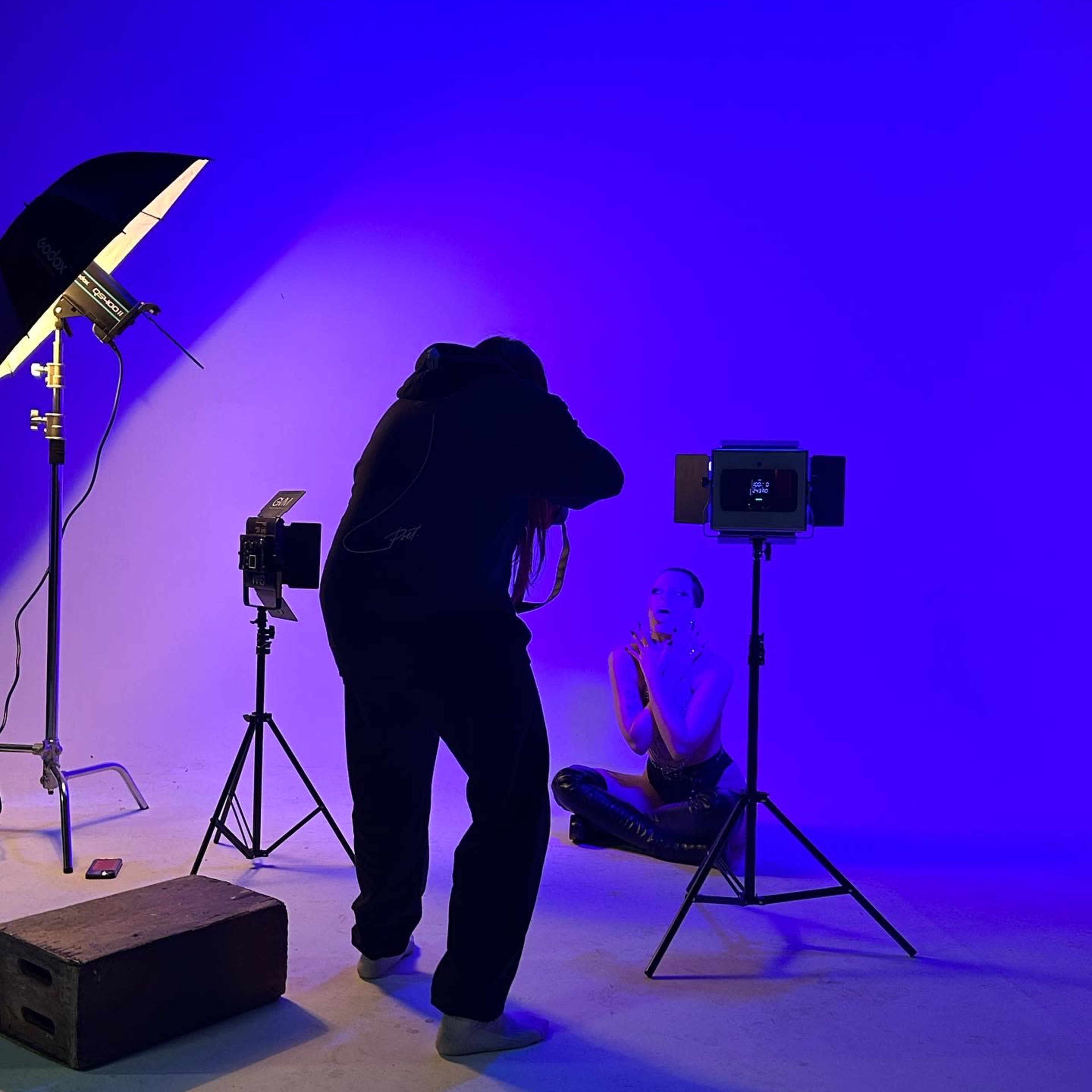 A photographer captures an image of a model posing under blue lighting in a studio setting.