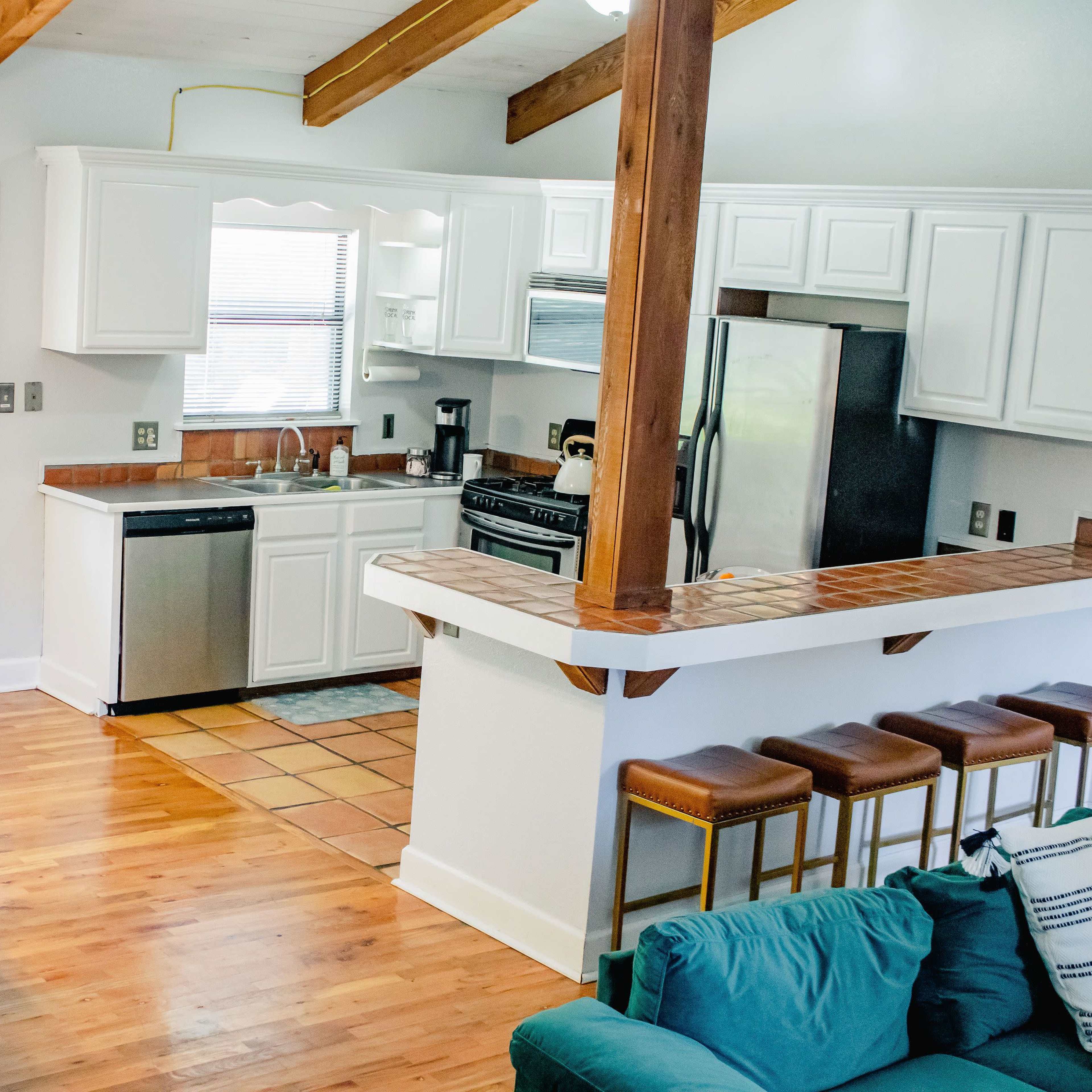A modern kitchen and dining area with white cabinetry, stainless steel appliances, a dining table set for four, and a living space featuring a green couch.