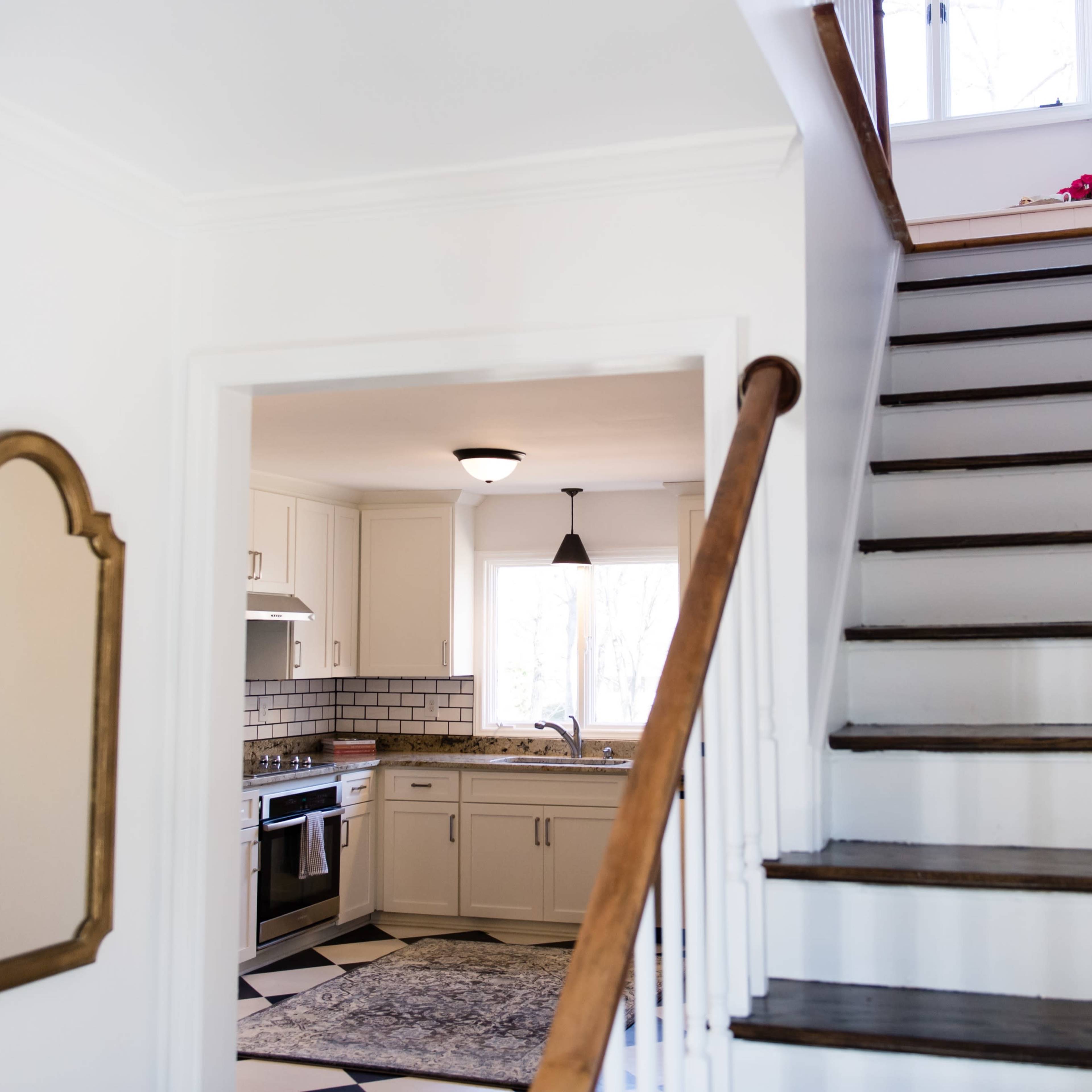 A well-lit home interior featuring a staircase leading to a second floor and an open kitchen visible through an archway.