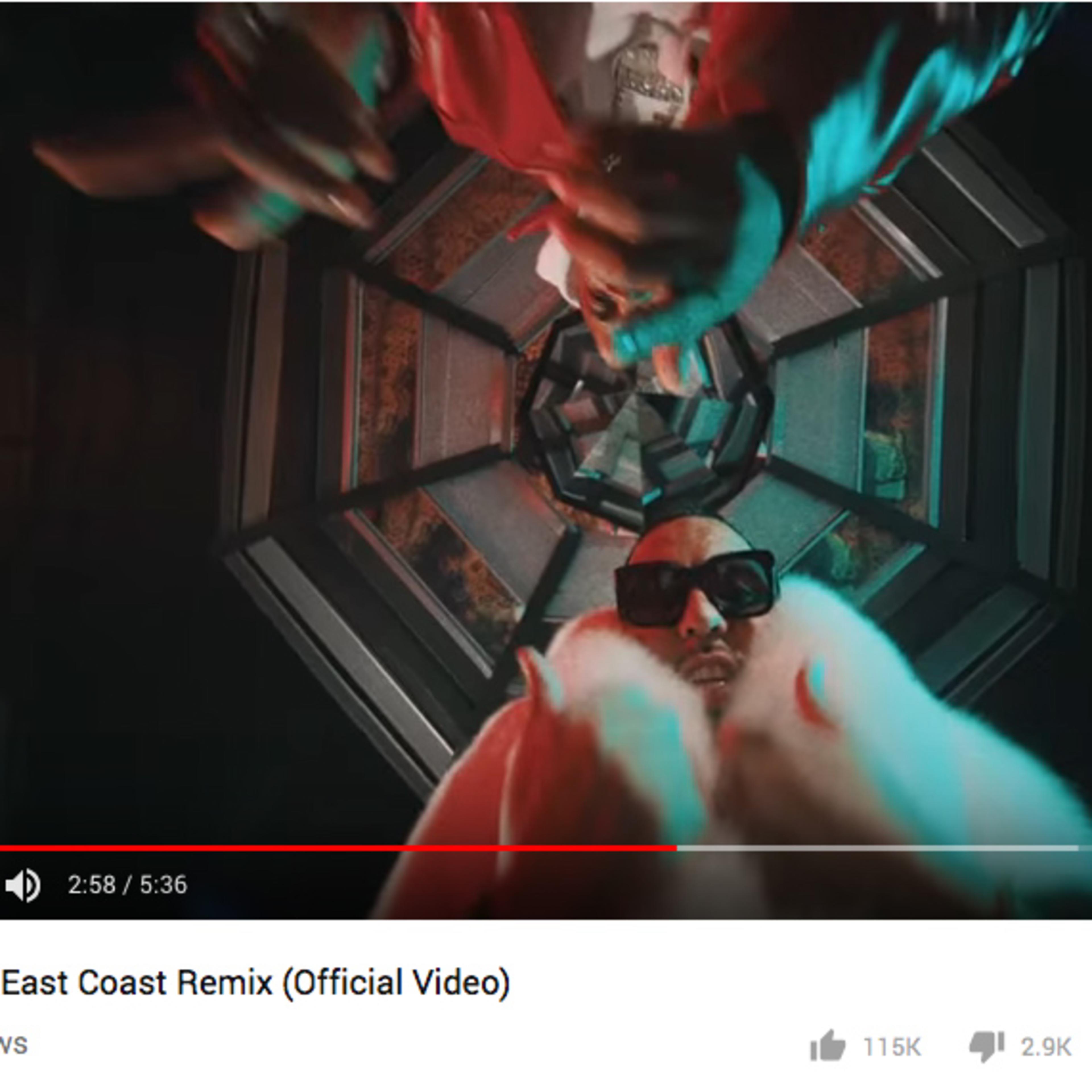 An artist wearing sunglasses and a fur coat, gesturing with his hands inside a vividly lit geometric space.