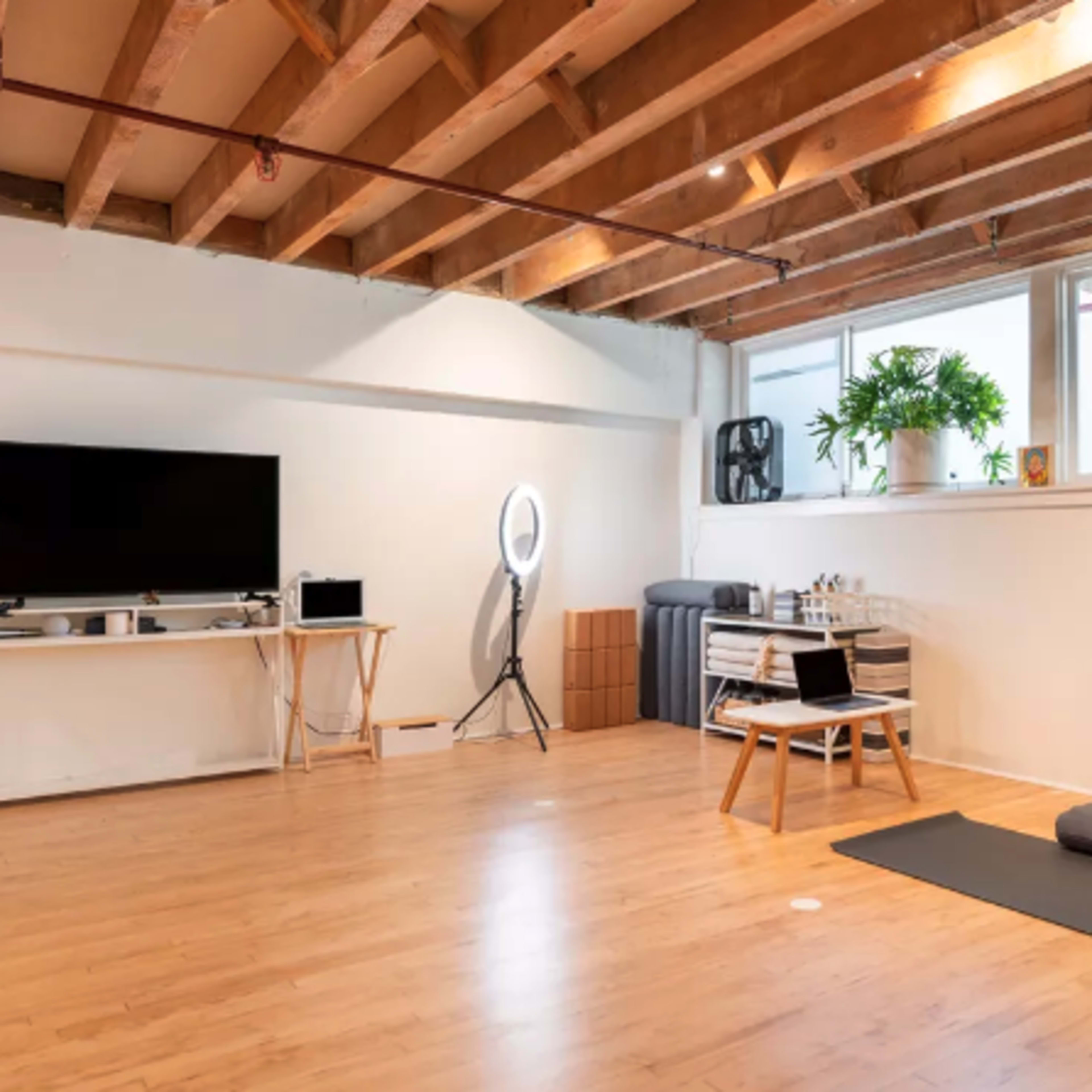 A minimalist room with hardwood floors features a large window, a television on a stand, a yoga mat, and a seating area with a table and chairs.