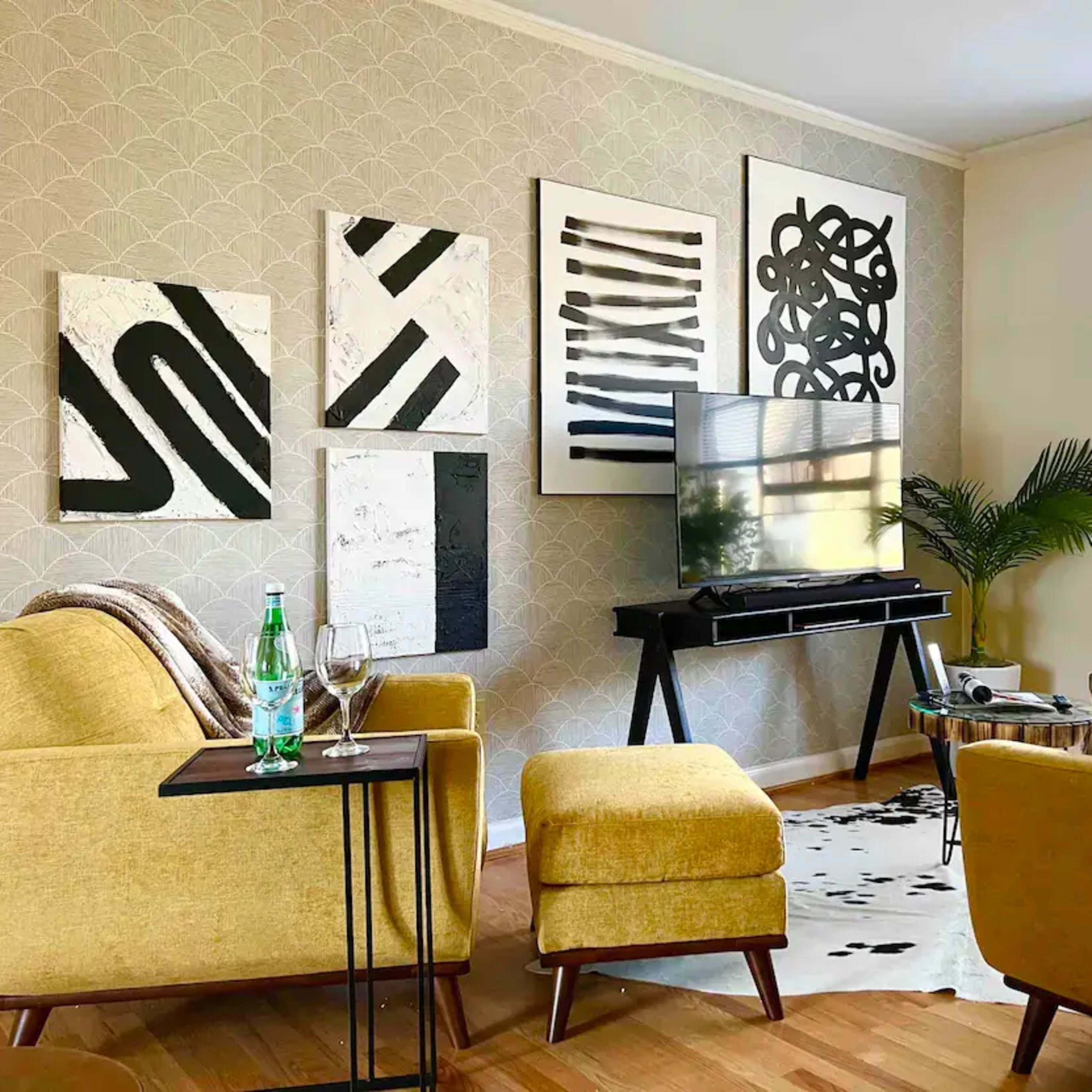 A modern living room featuring yellow furniture, black and white abstract wall art, and a television on a sleek stand.