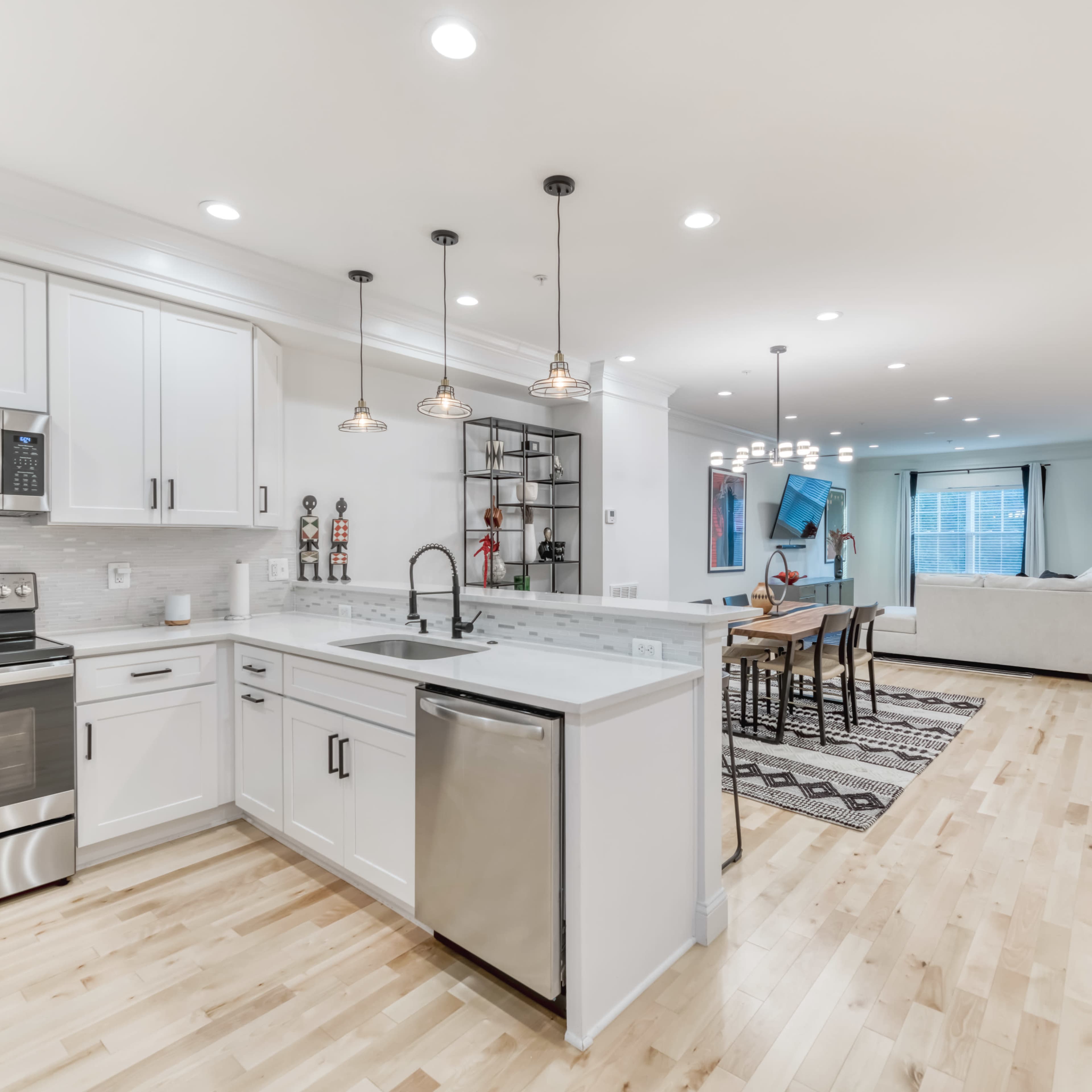 A modern kitchen with white cabinetry, stainless steel appliances, and a large island, leading into an open-concept living area.