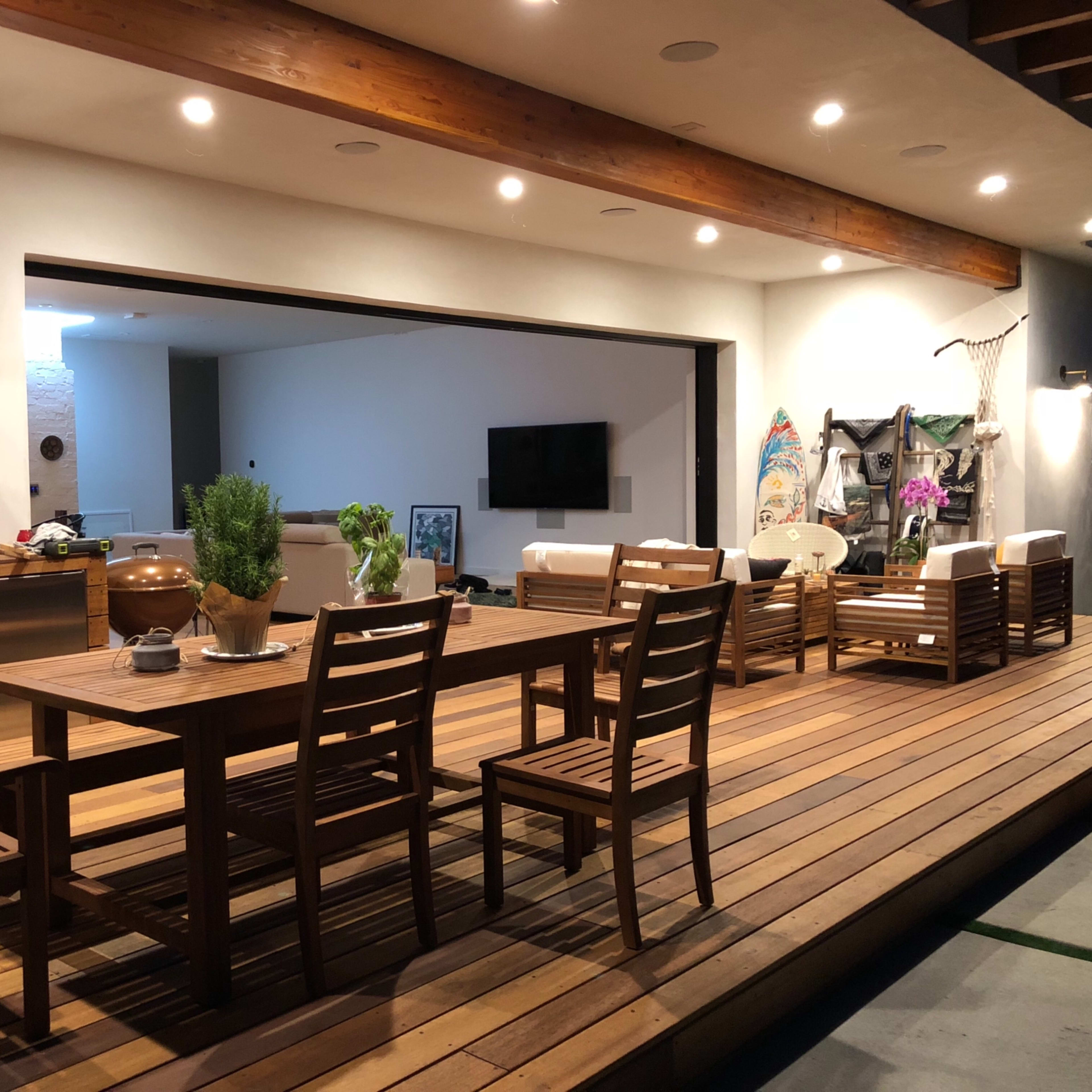 A modern outdoor dining area with a wooden table, chairs, a grill, and a seating arrangement under a covered patio.