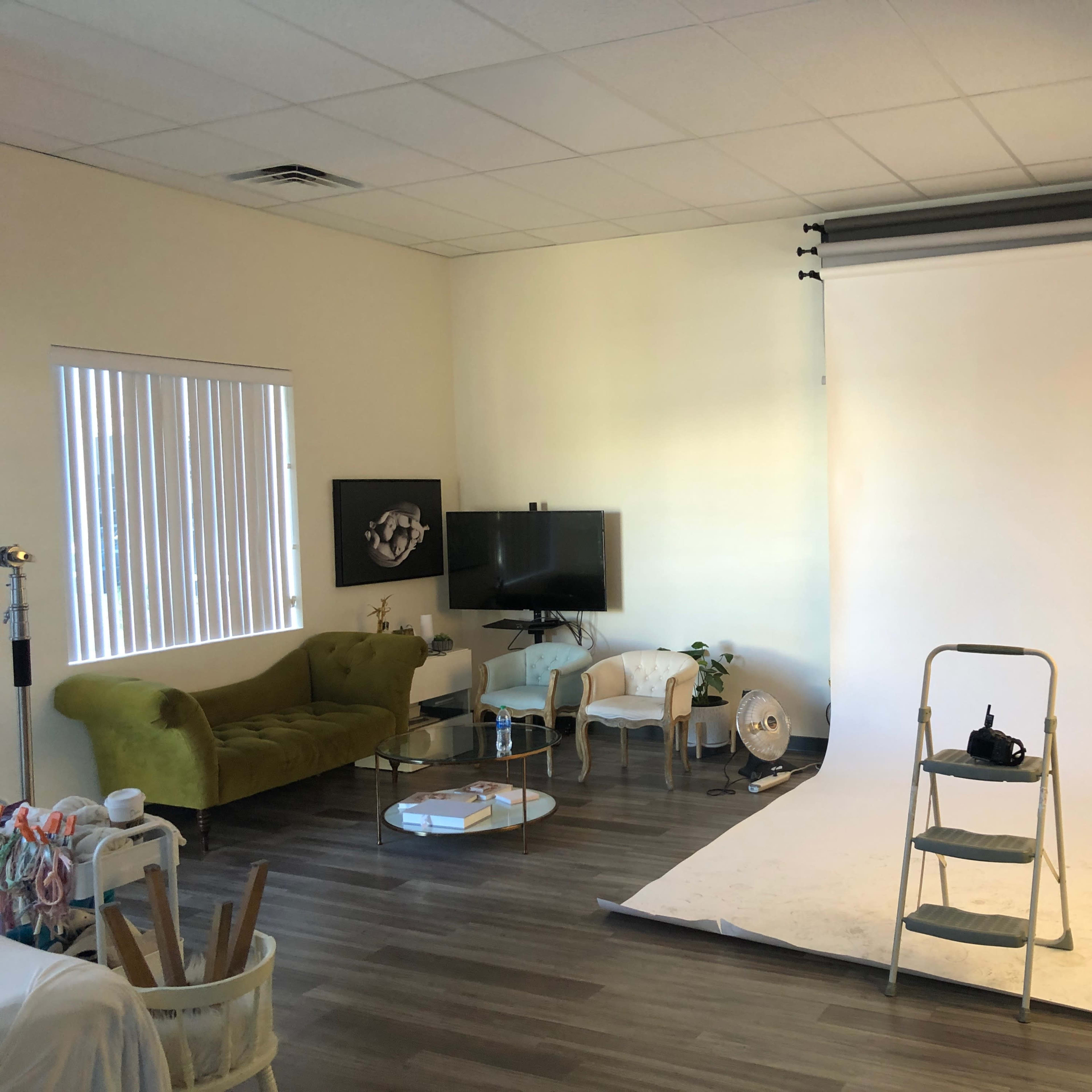 A photography studio with a green sofa, a television, and a backdrop setup featuring a step ladder.