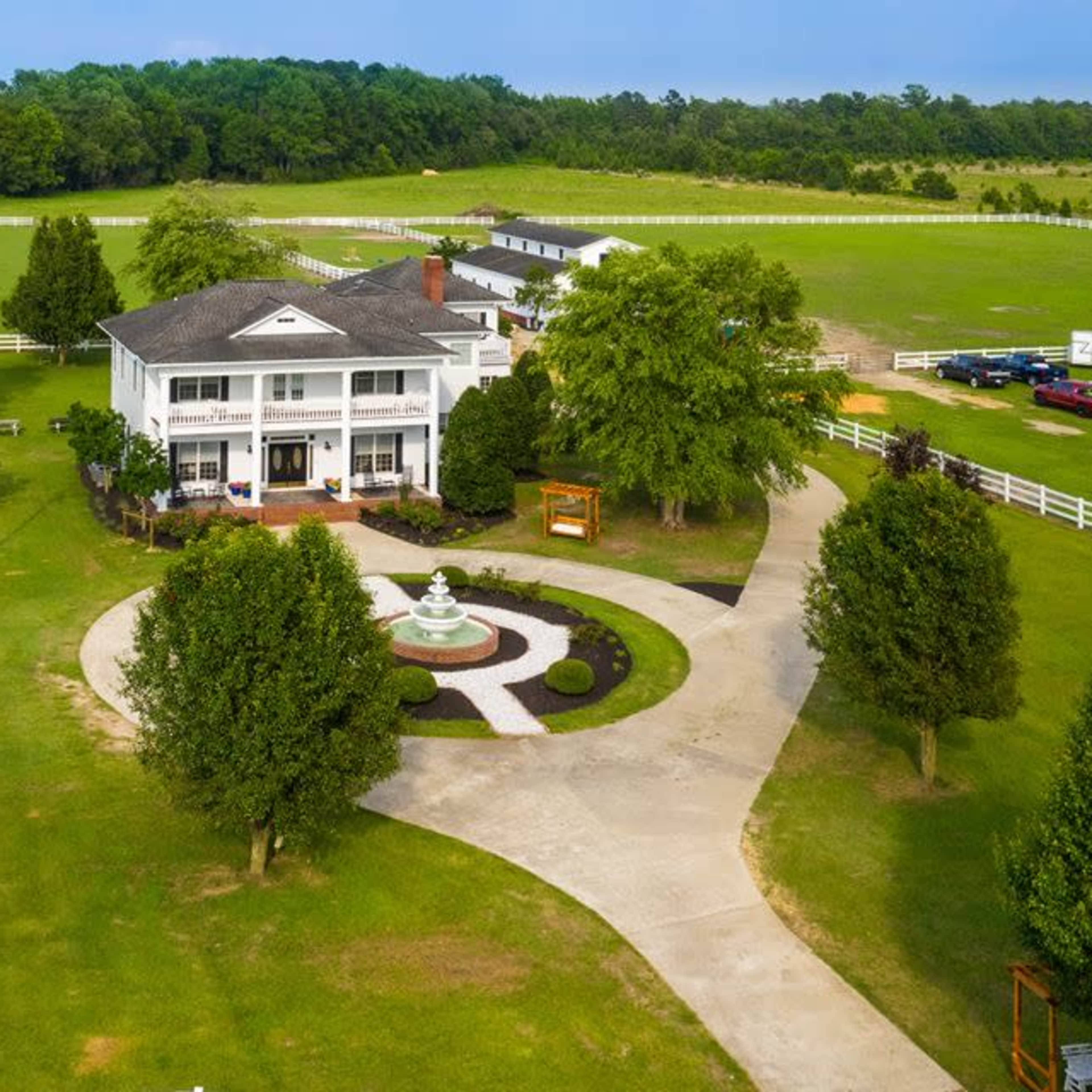 A large, two-story white house with a circular driveway, surrounded by landscaped lawns and trees.