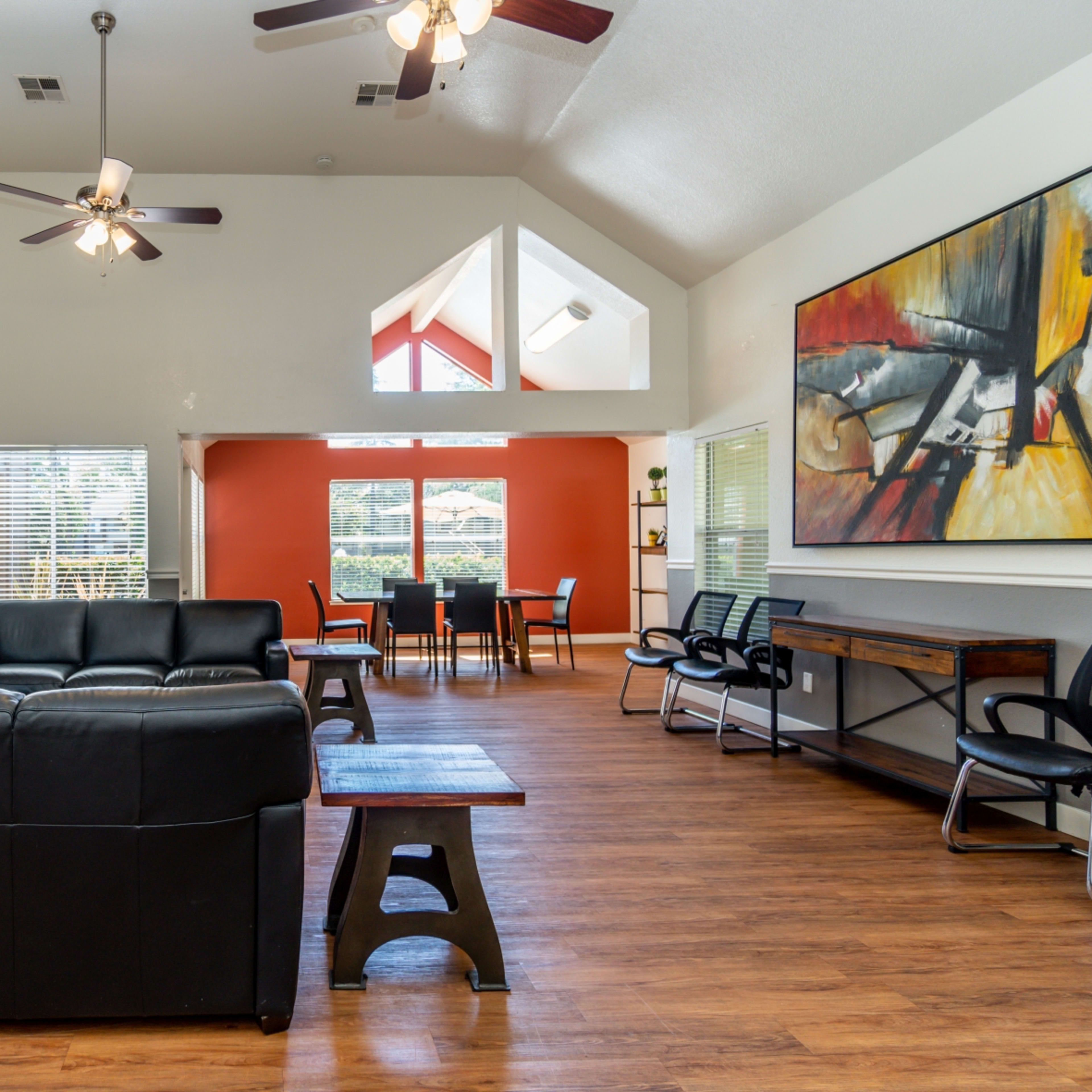 A spacious living area featuring black leather furniture, a stone accent wall, large windows, and a wooden floor.