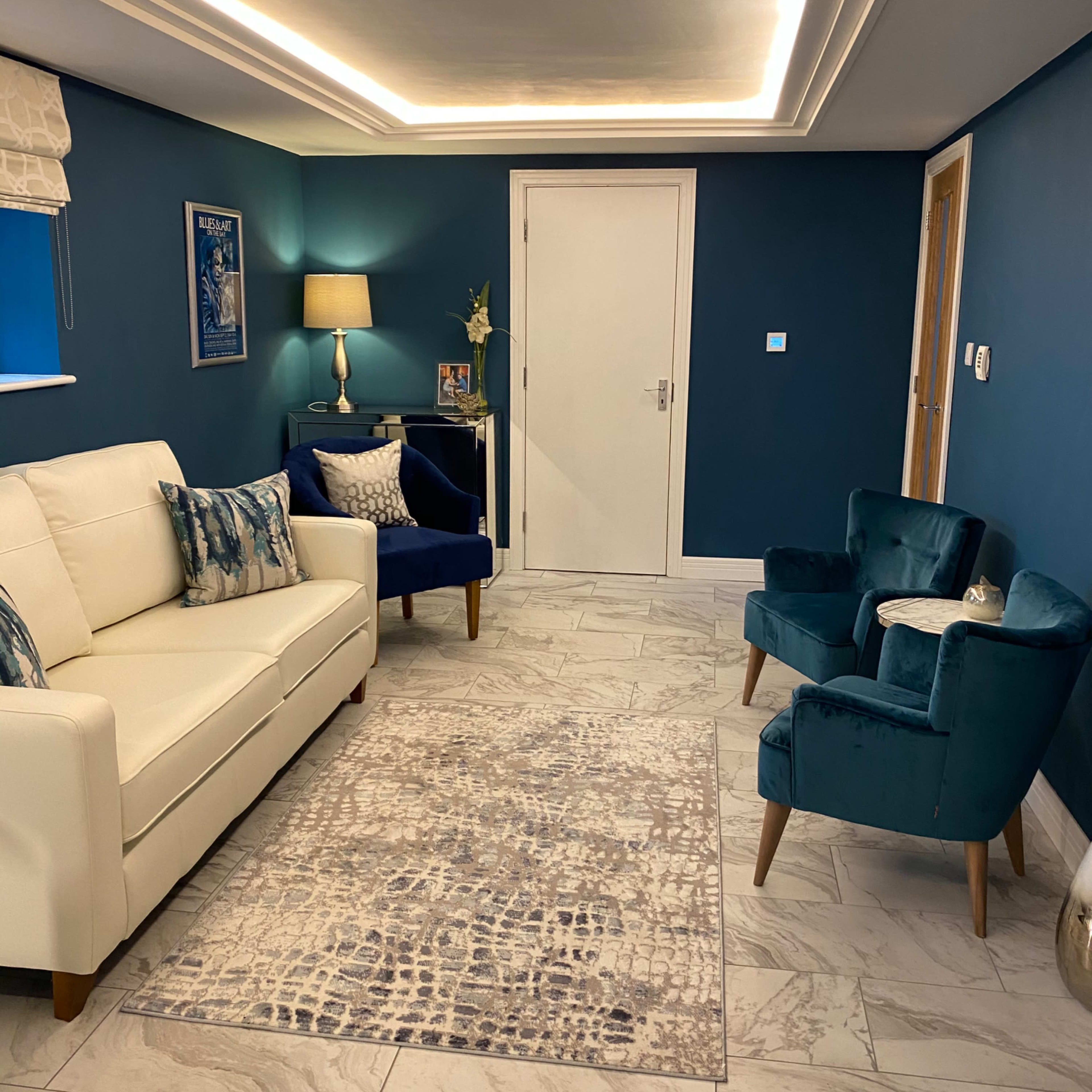A living room featuring a white sofa, a blue armchair, a decorative rug, and a sliding door, complemented by recessed lighting and a lamp.