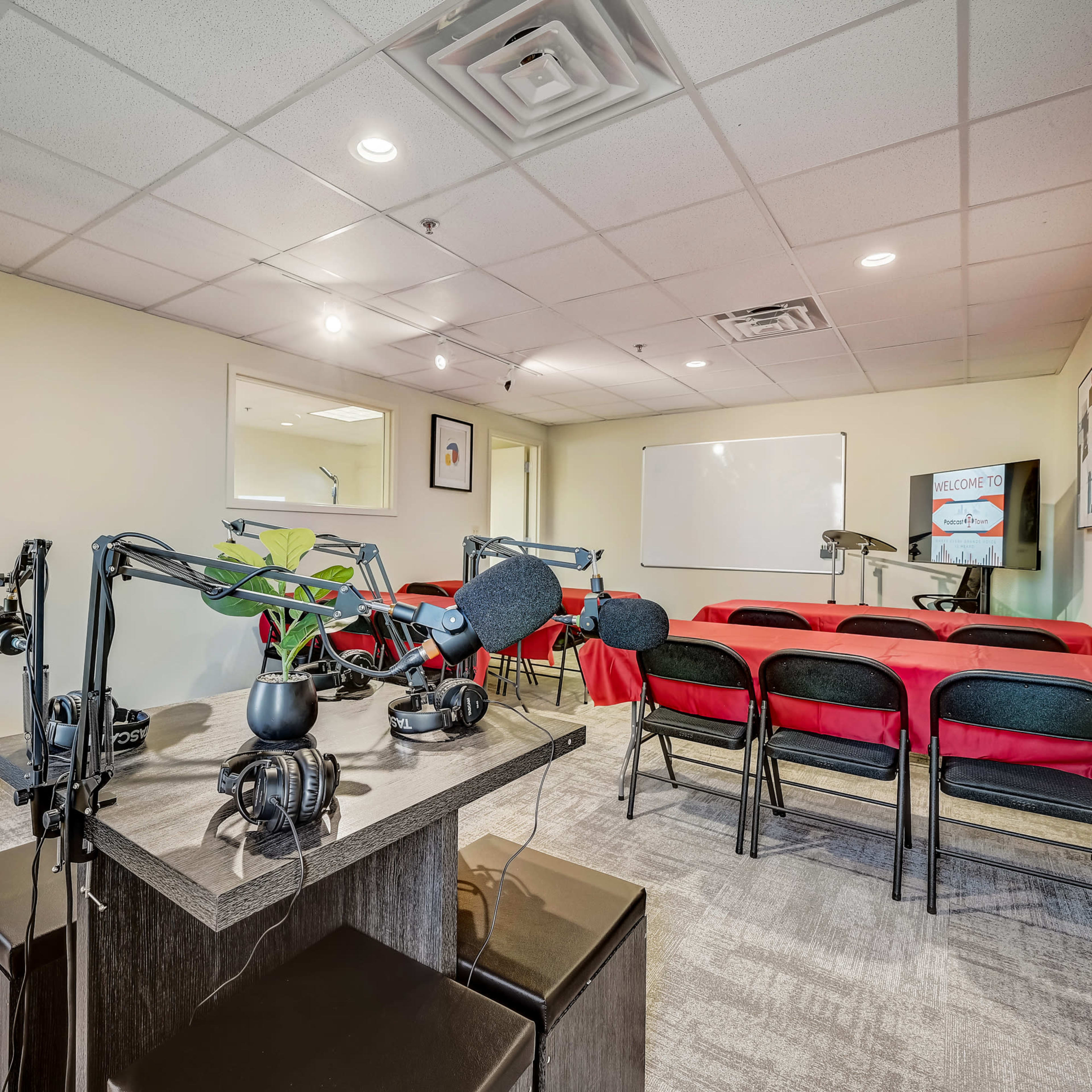 A small conference room equipped with a black table and chairs, a whiteboard, and a podcasting setup featuring microphones and headphones.