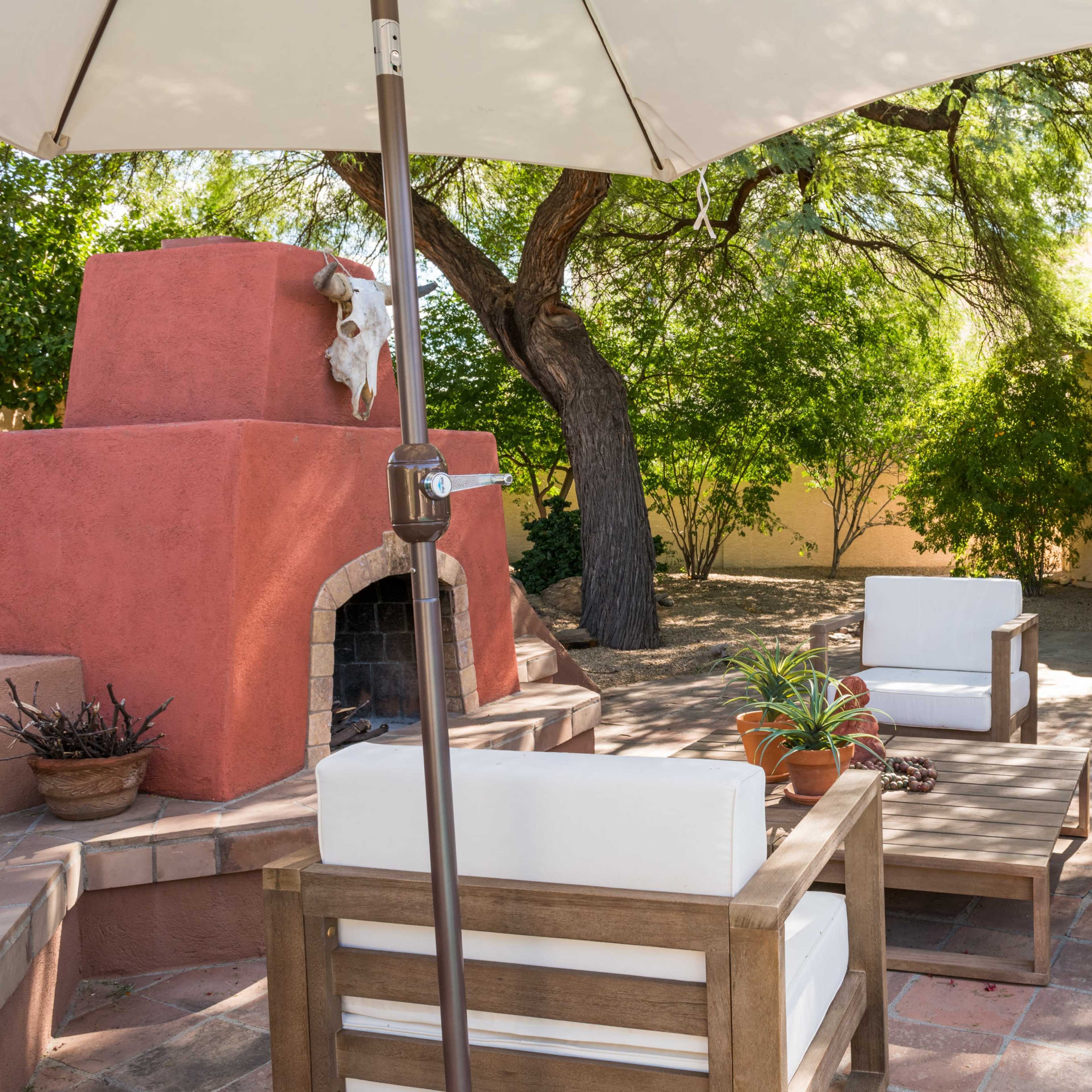 A backyard patio with a fireplace, seating area, and an outdoor grill surrounded by greenery.
