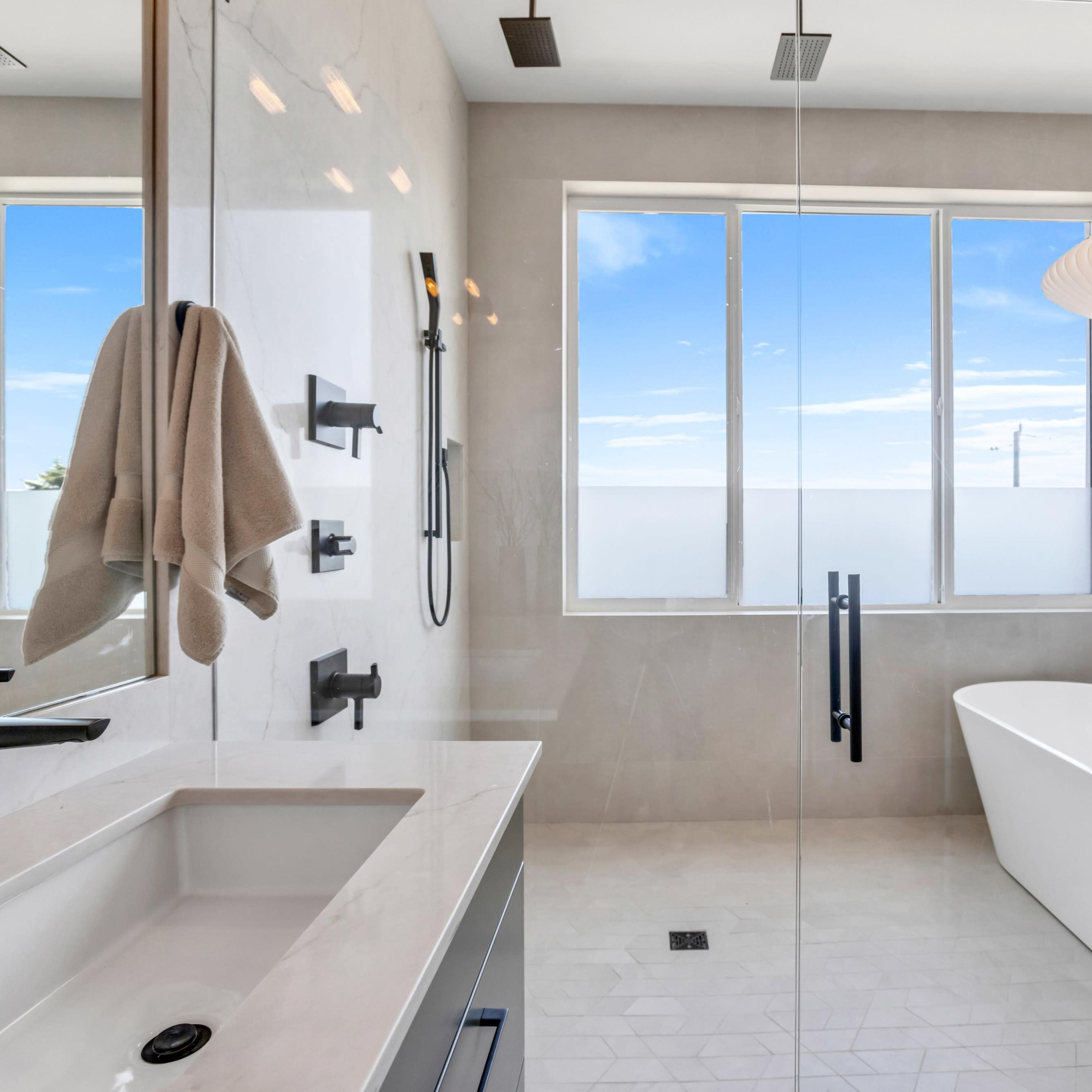 The bathroom features a modern design with a freestanding tub, a dual sink vanity, and large windows that provide natural light.