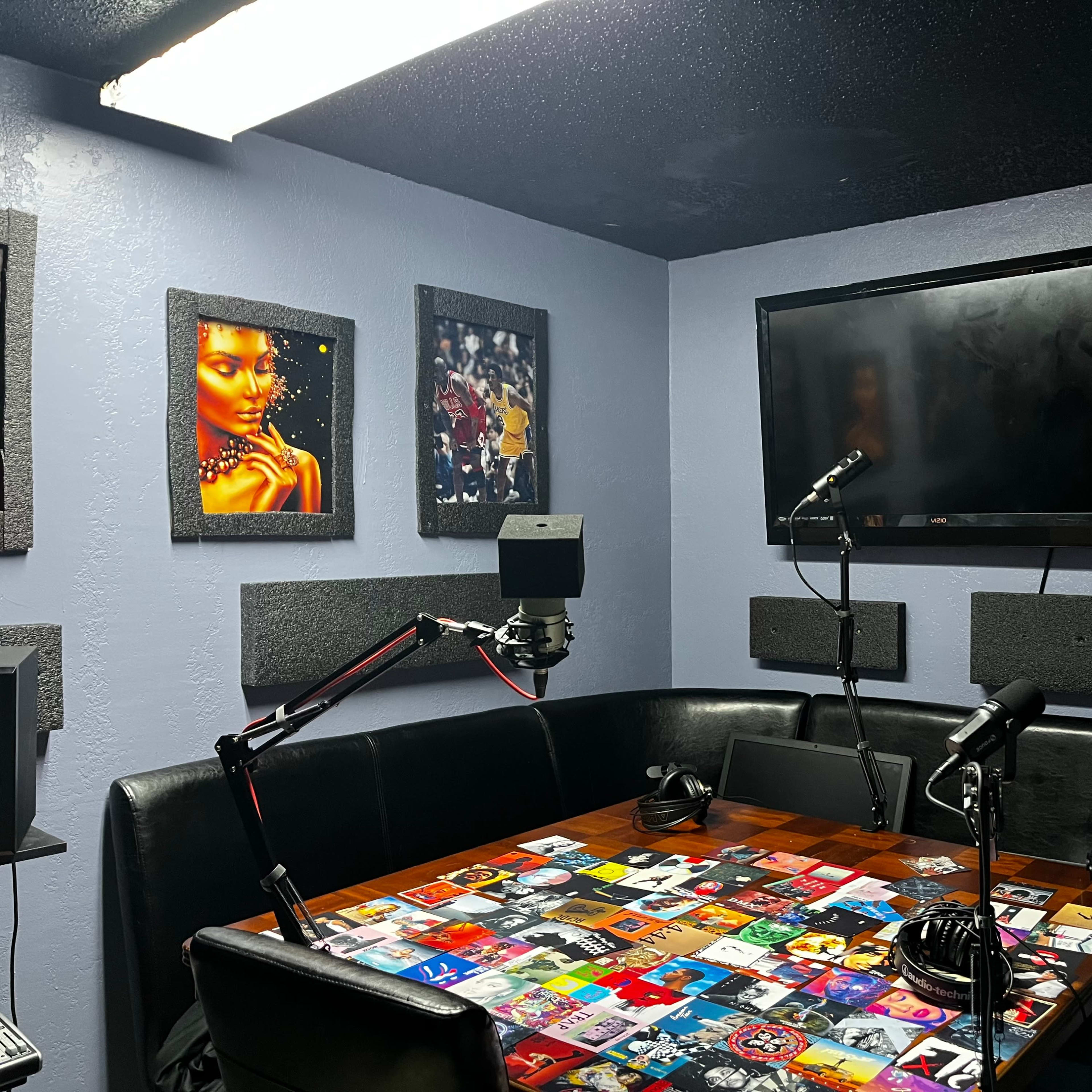 A recording studio with a table covered in album covers, microphones on stands, and art displayed on the walls.