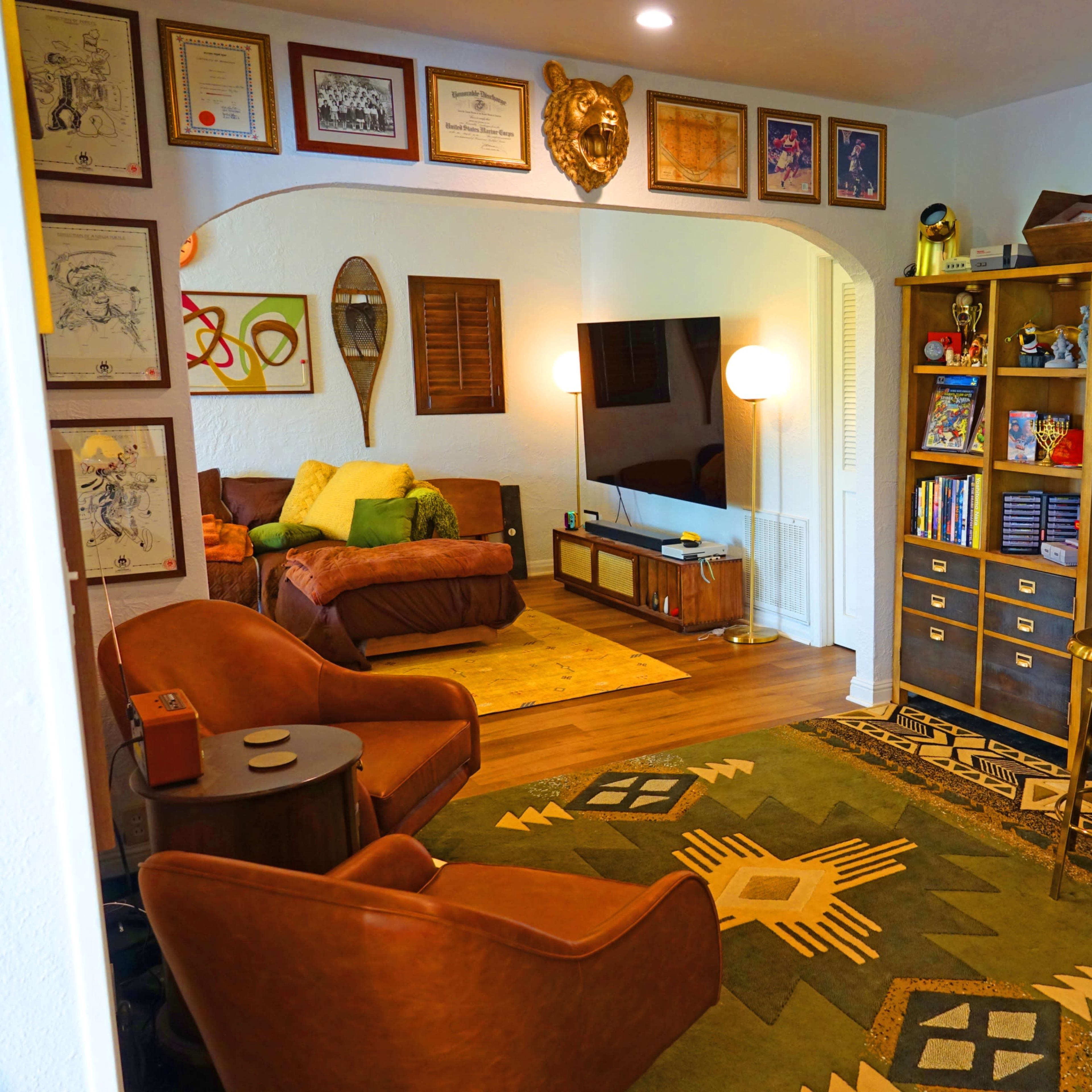 A cozy living room with a retro arcade cabinet, a comfortable seating area, and framed artwork on the walls.