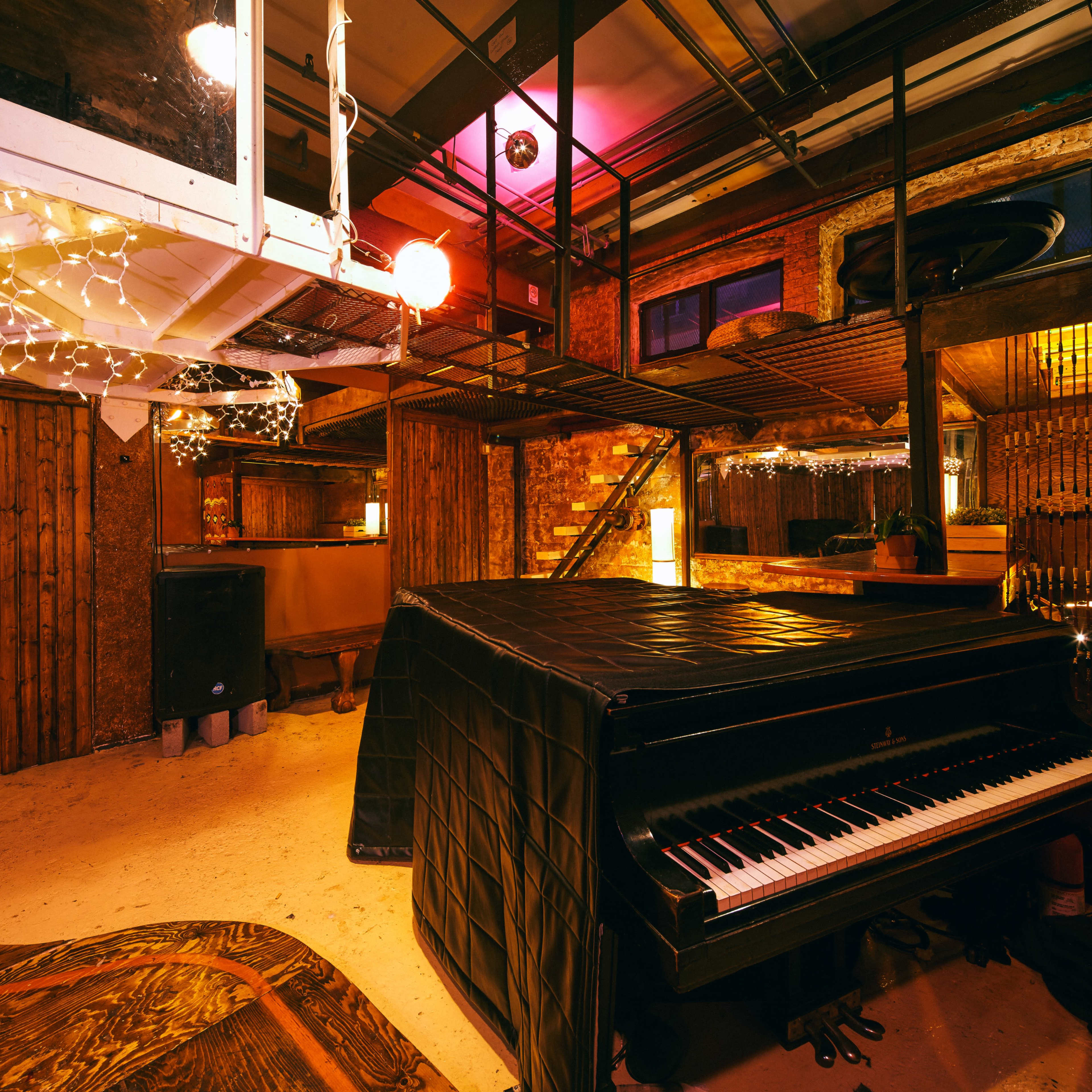 A dimly lit music studio featuring a black grand piano covered with a protective sheet, surrounded by wooden walls and industrial decor.