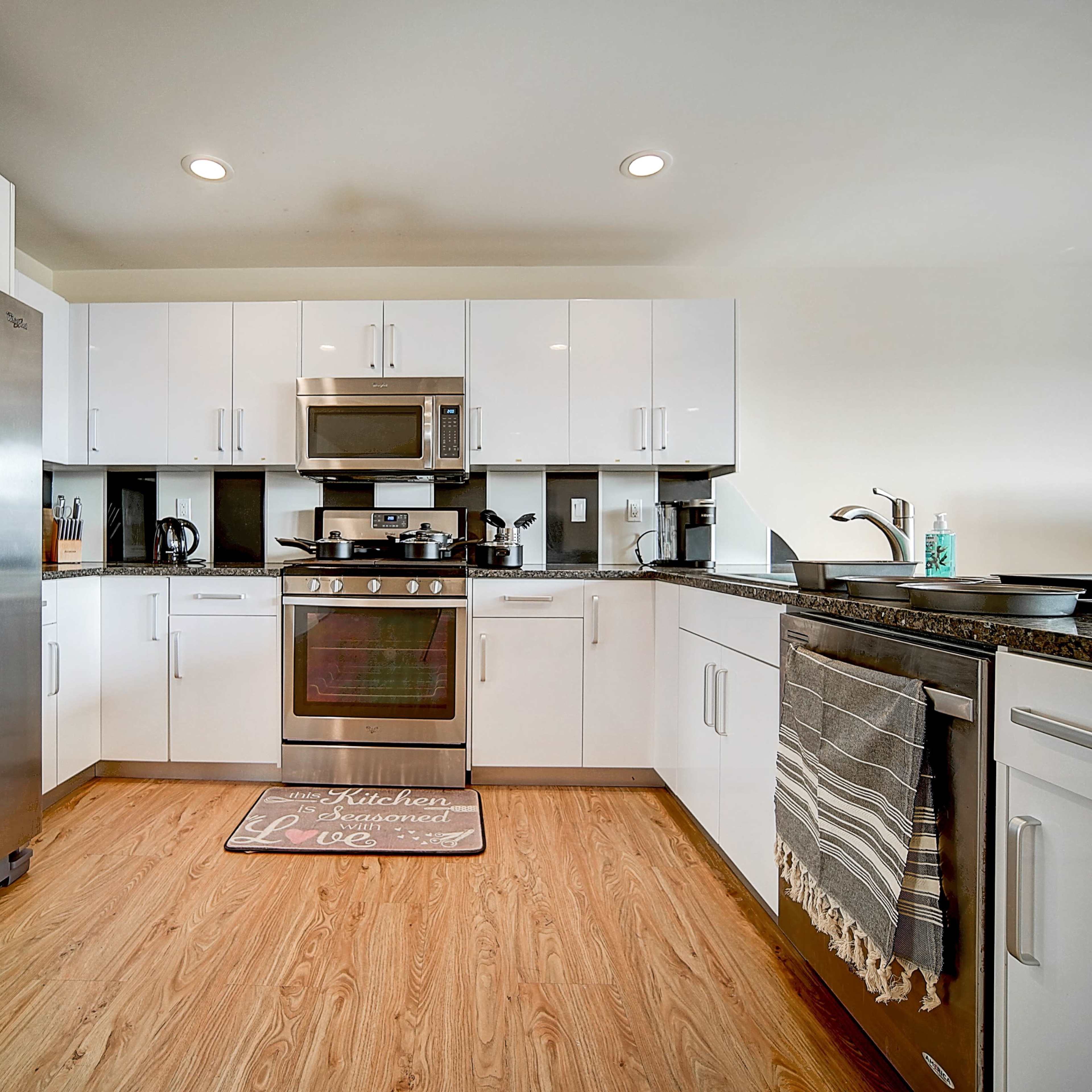 A modern kitchen features stainless steel appliances, white cabinetry, and a granite countertop with a textured rug on the floor.