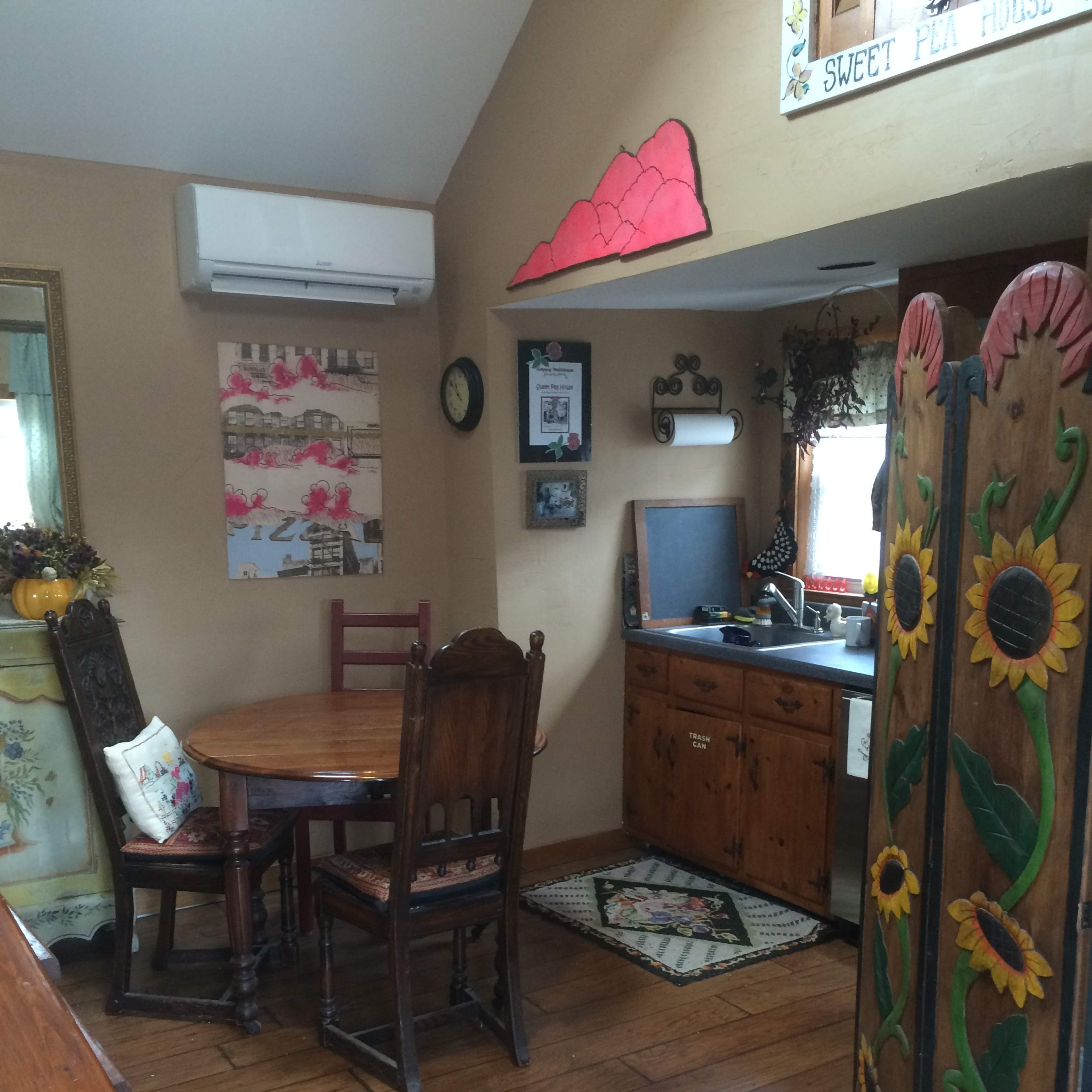 A small dining area with a wooden table and chairs, a kitchen sink, and a decorative partition featuring sunflowers.