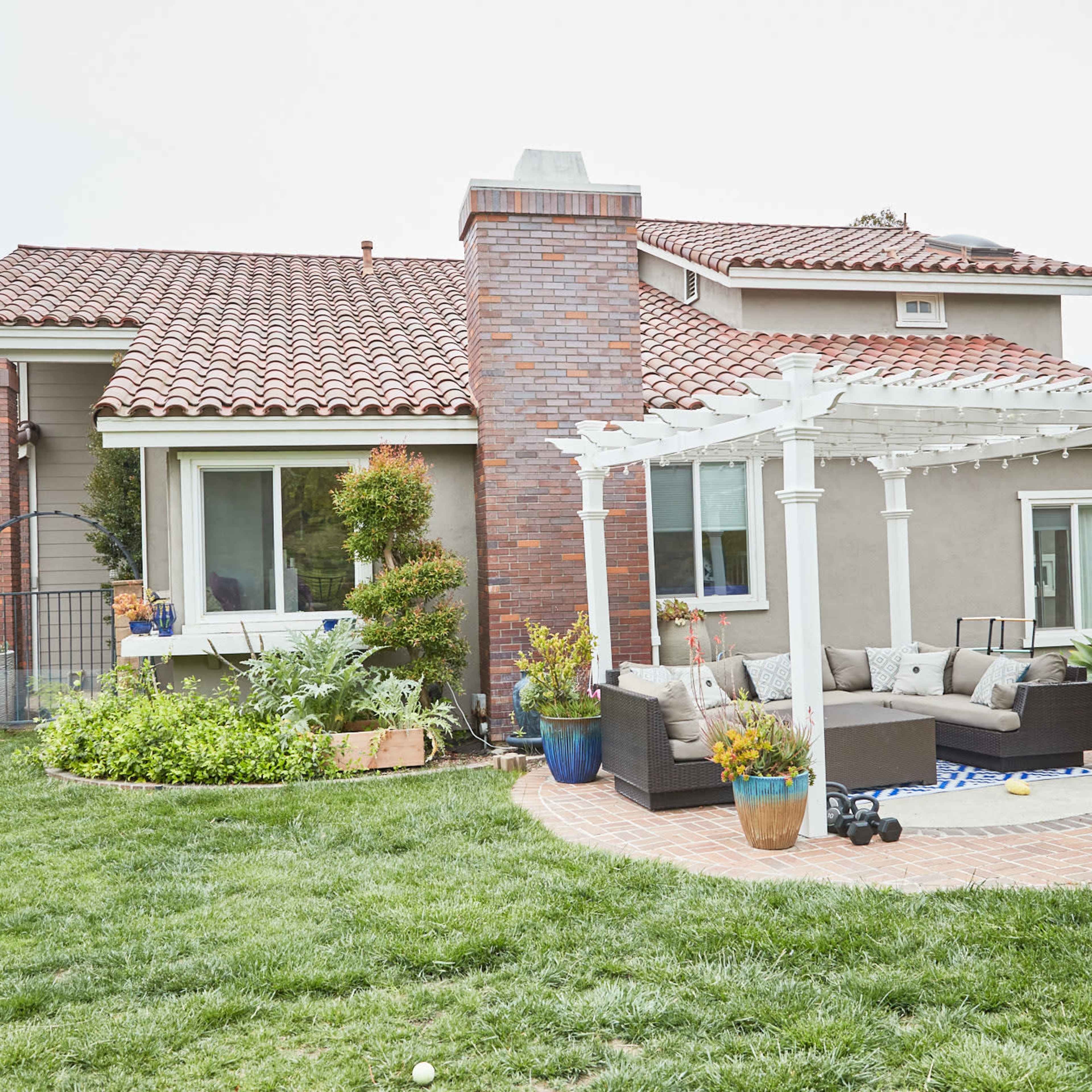 A modern house with a landscaped backyard featuring a pergola over a seating area and a well-maintained lawn.