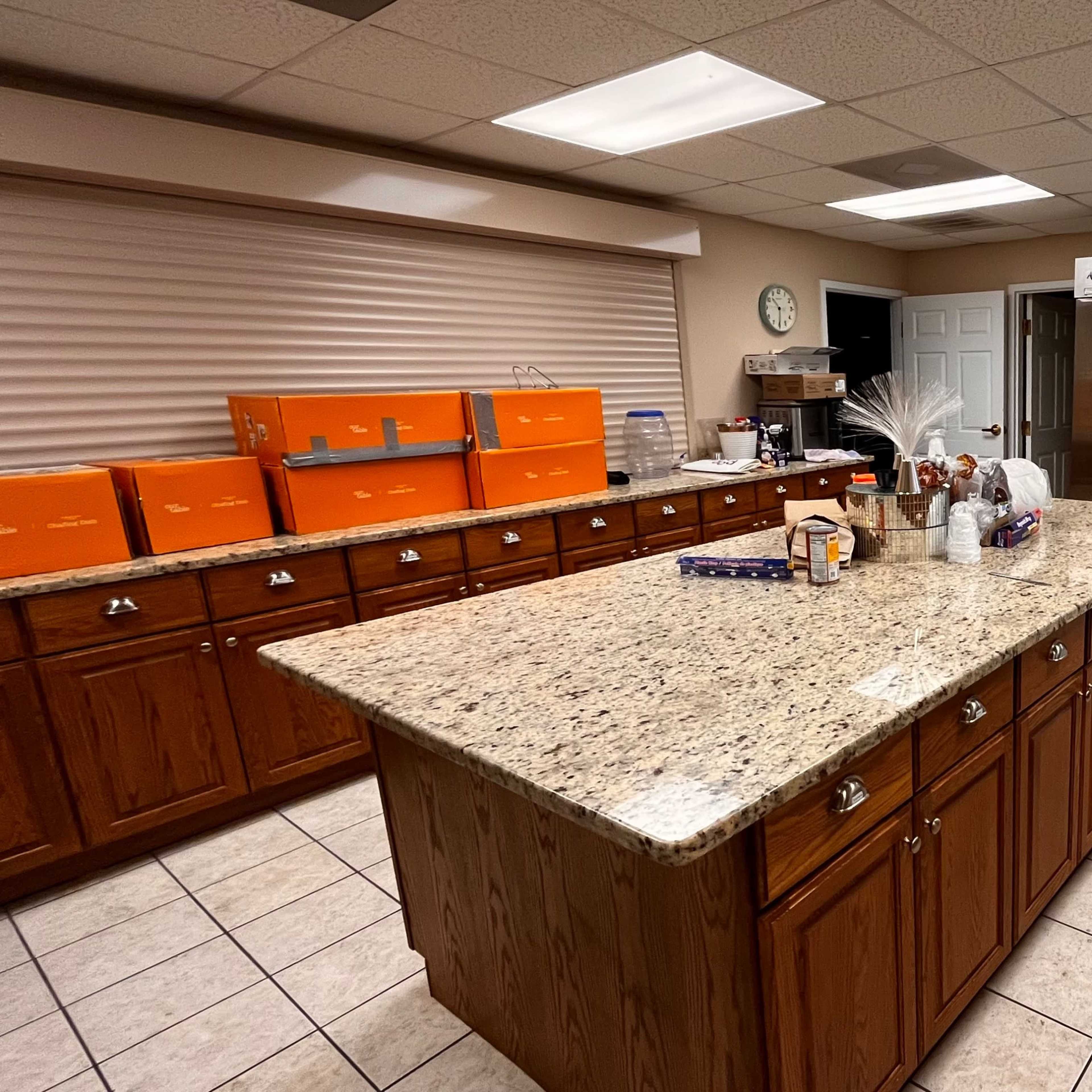 A spacious kitchen with wooden cabinets, a large granite island in the center, and stainless steel appliances, including a refrigerator and a second white refrigerator.