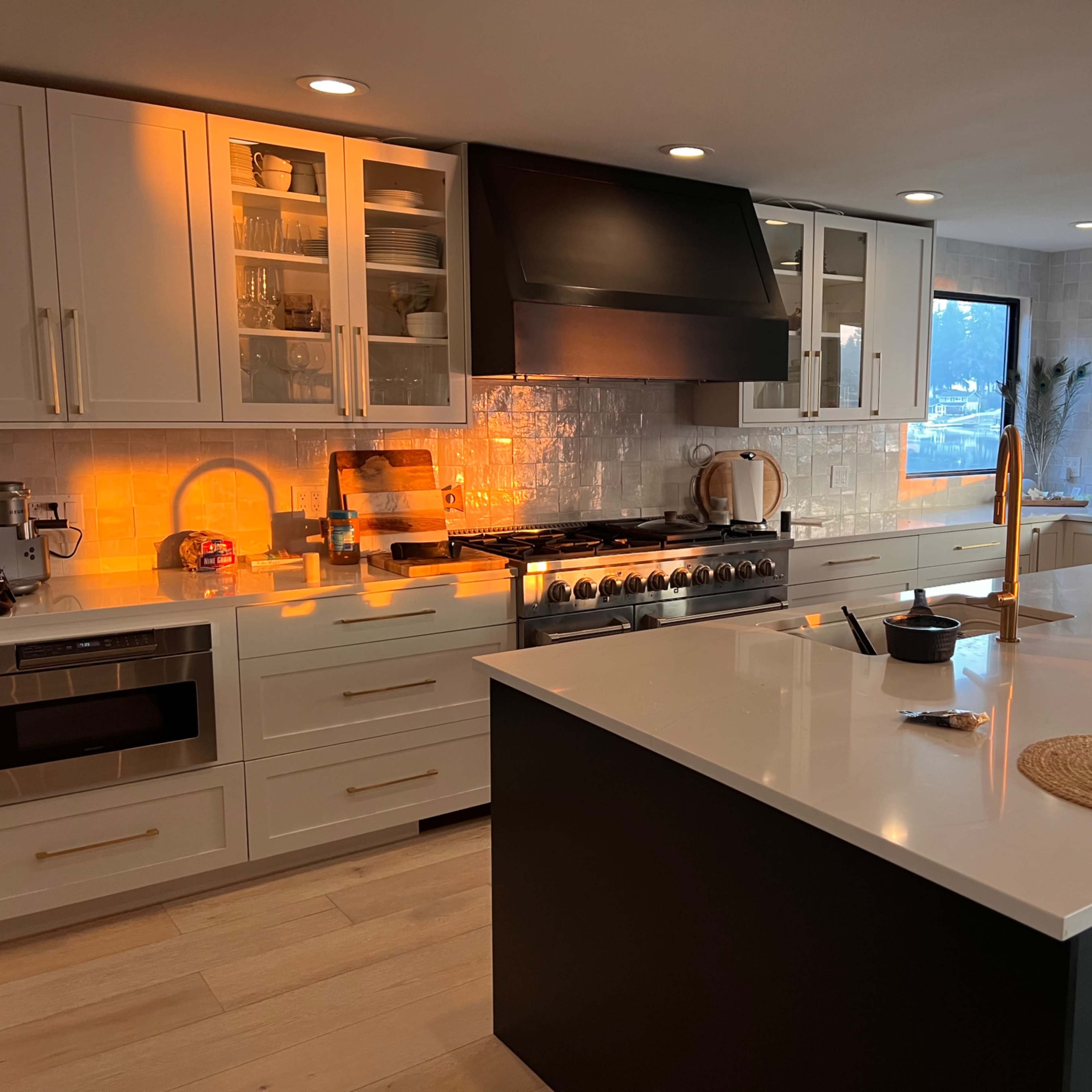 The kitchen features white cabinets, a large island with a dark base, a professional-grade stove, and warm lighting illuminating the workspace.