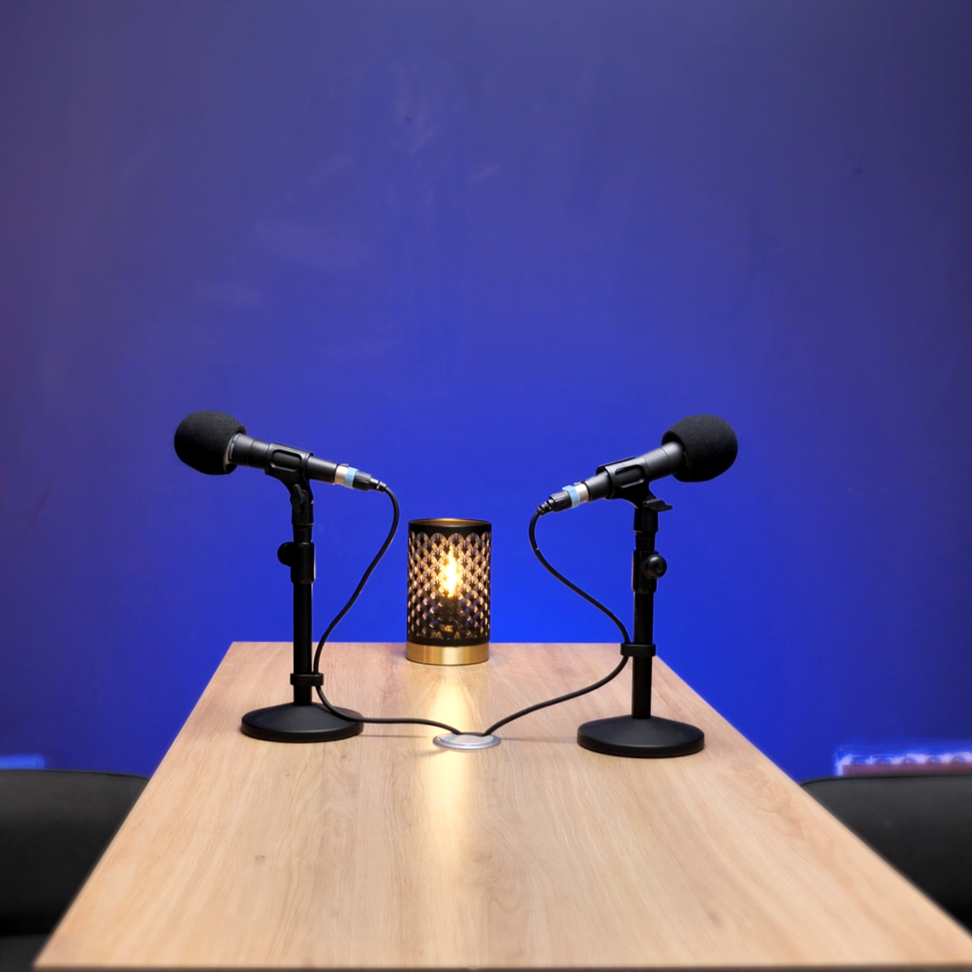 A wooden table with two microphones and a lantern is set against a blue backdrop.