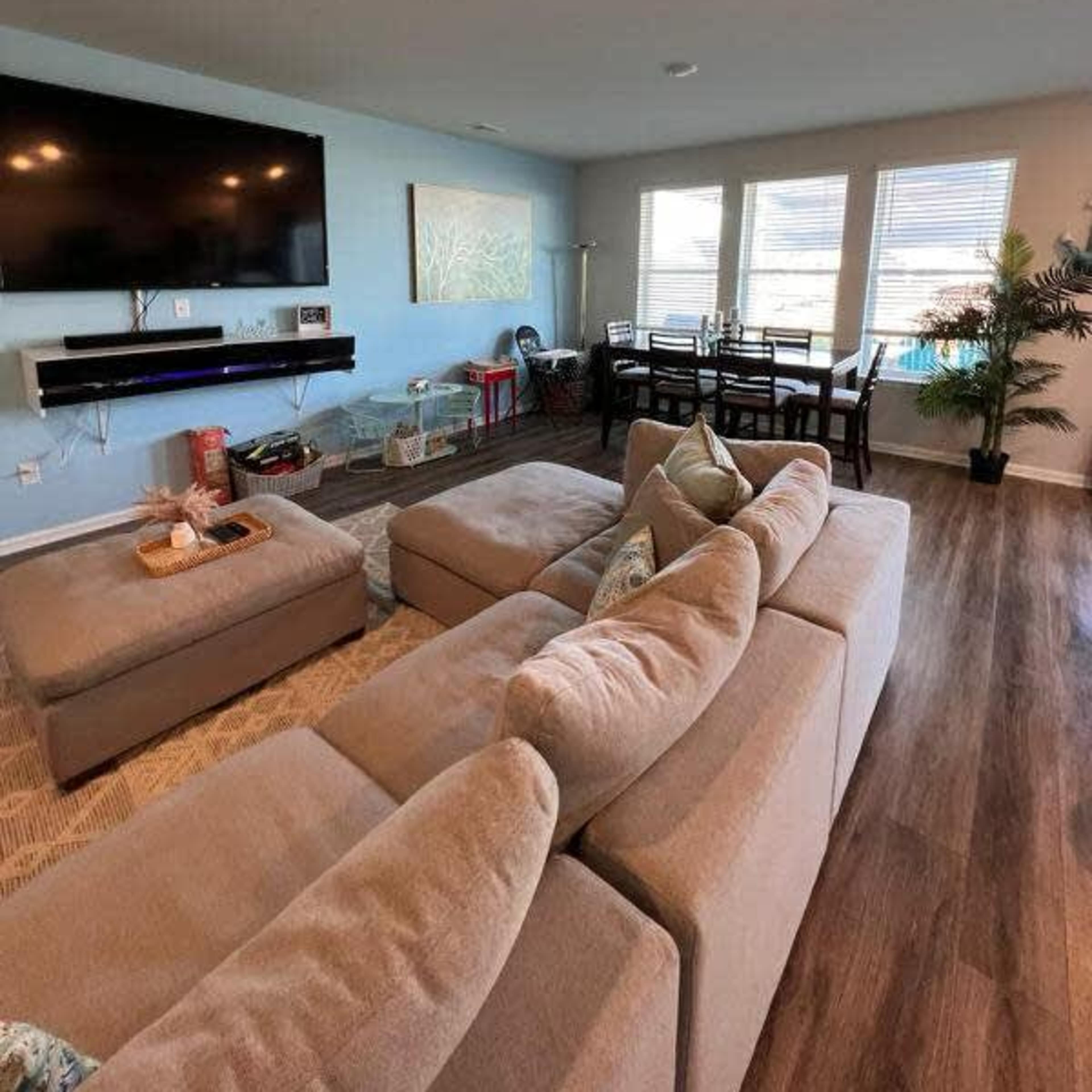 A cozy living room with a large sectional sofa, a wall-mounted television, and a dining area featuring a wooden table and chairs.