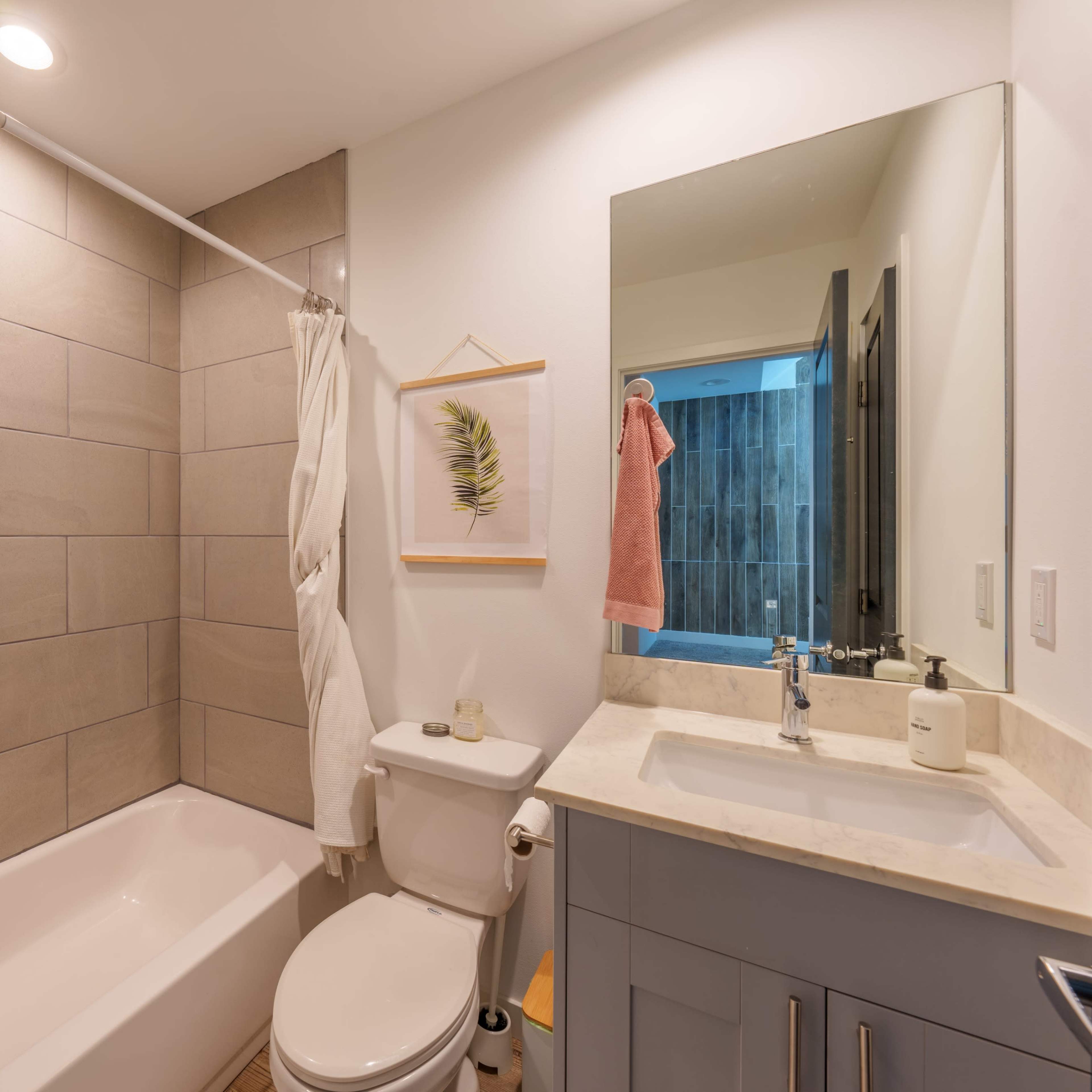 The bathroom features a shower/tub combination, a toilet, and a sink with a counter, all set against a backdrop of tiled walls.
