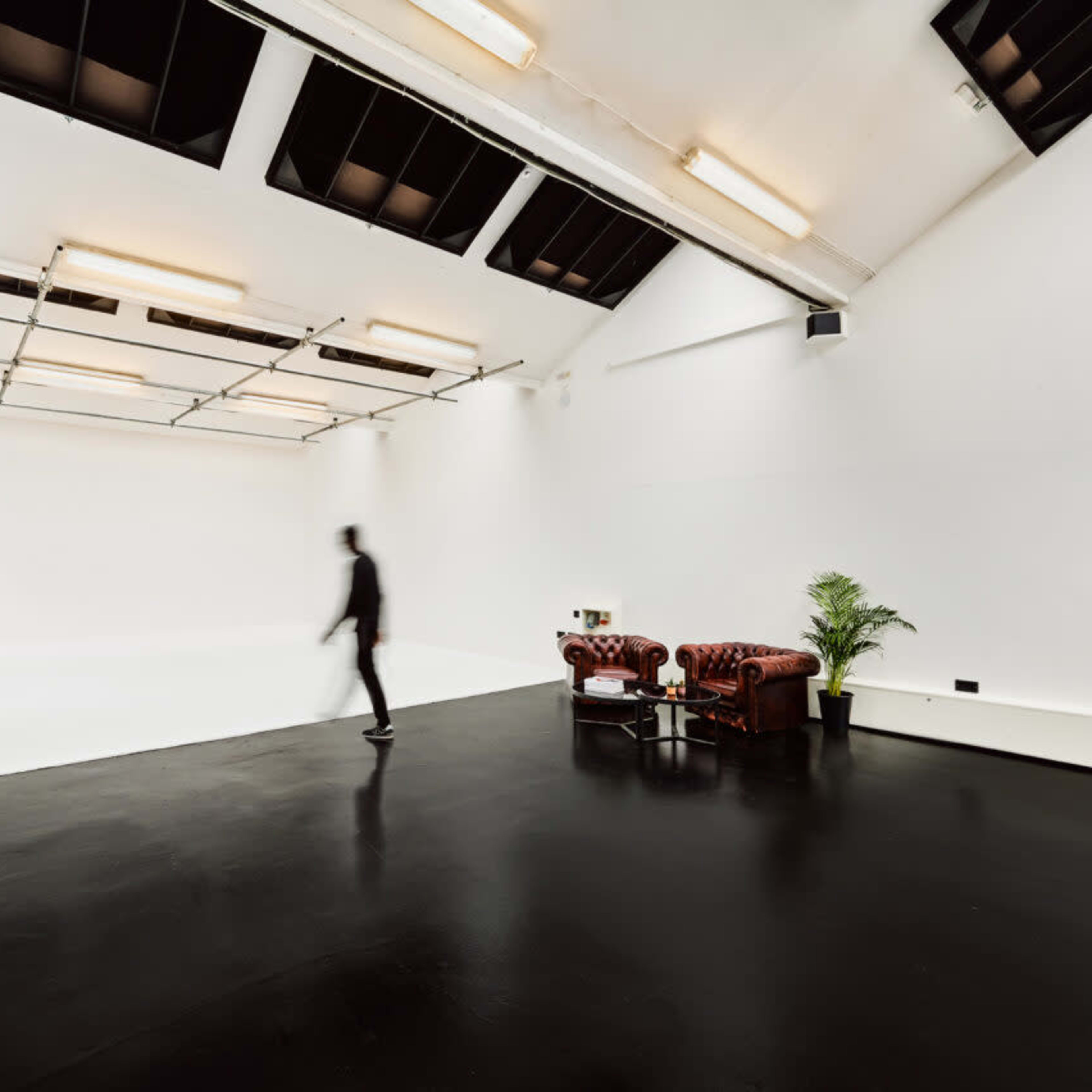 A person walks through a spacious, minimalist studio featuring a black floor and a brown leather couch.