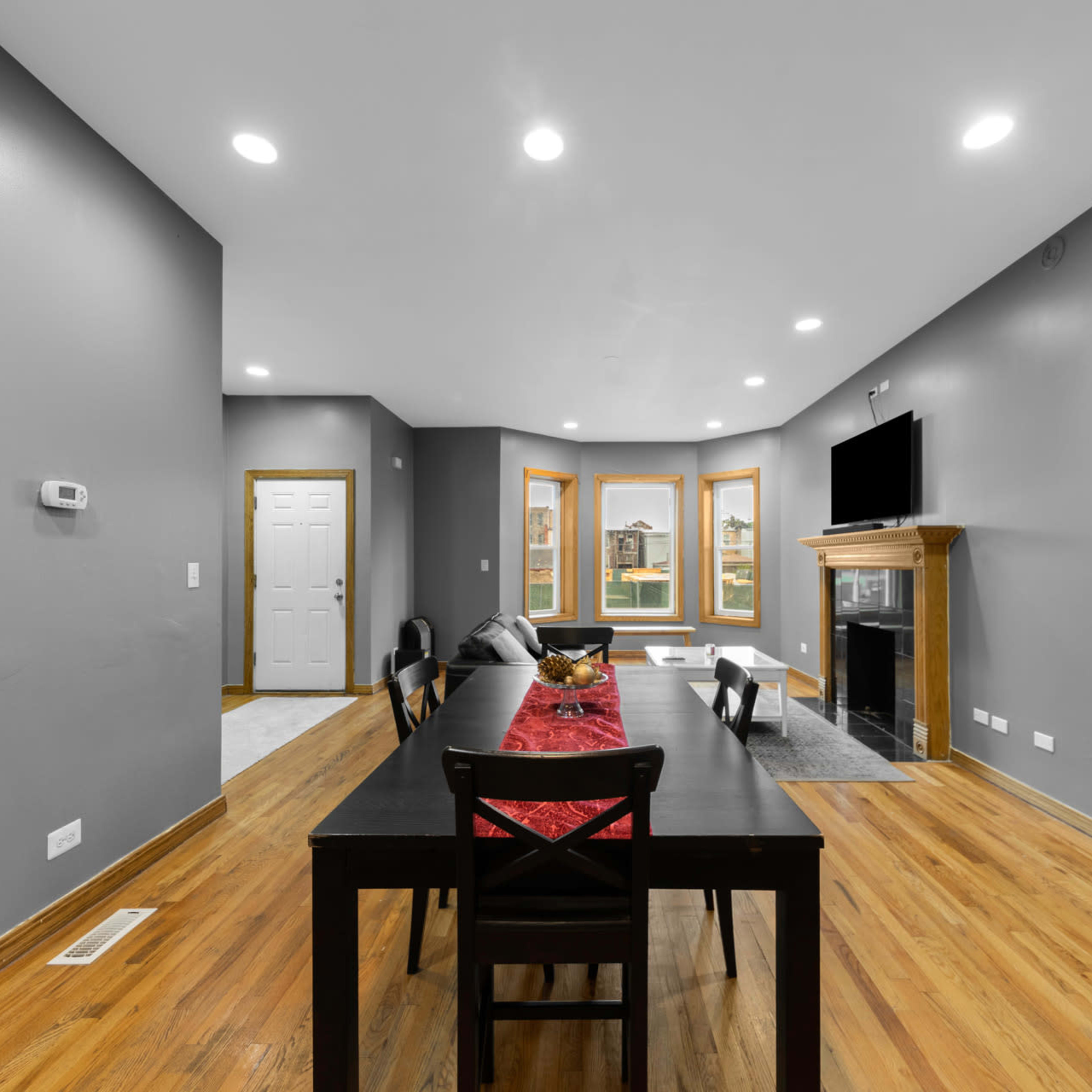 A spacious living area featuring a dining table with chairs, a fireplace, and large windows that provide natural light.