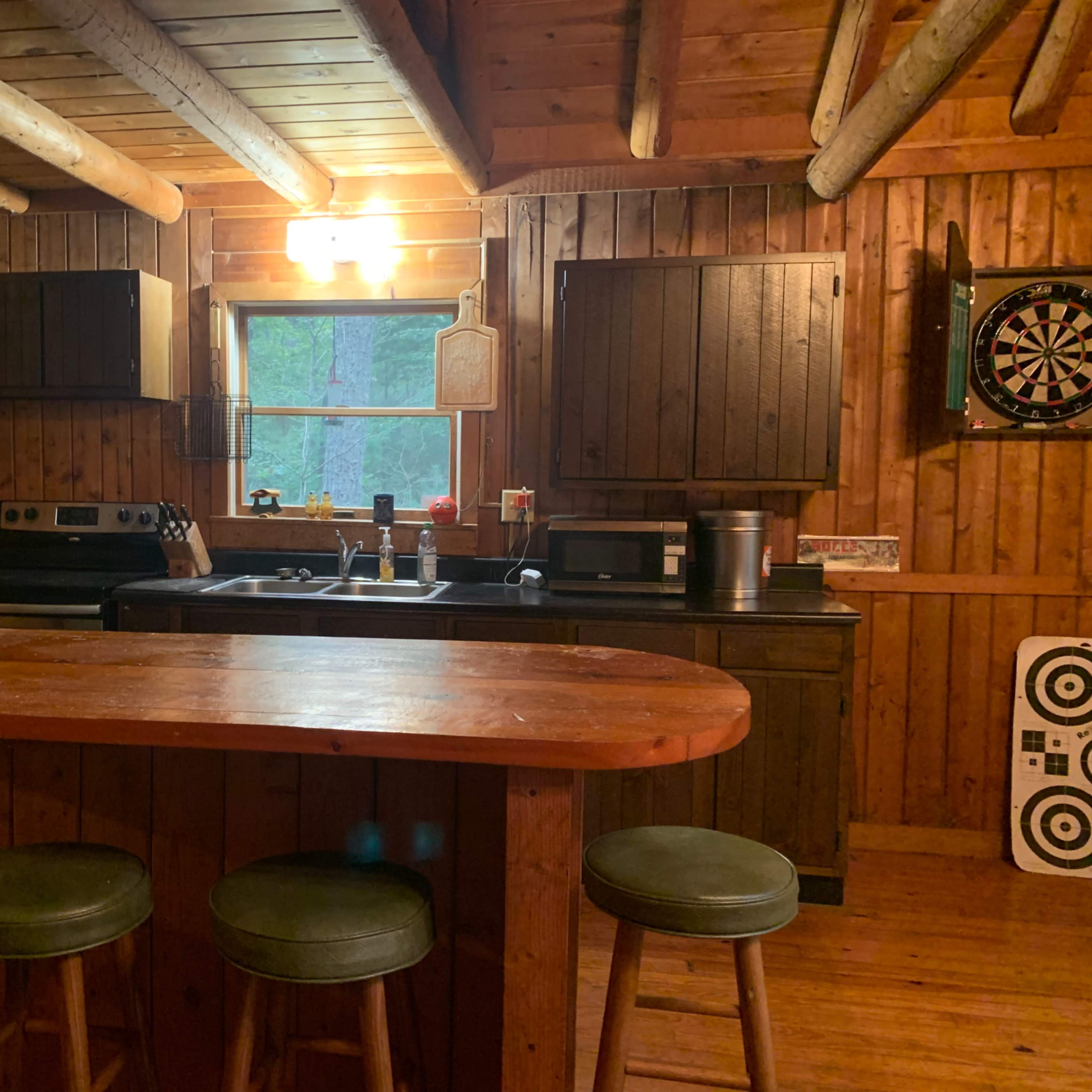 A rustic wooden kitchen with dark cabinets, a stove, and a bar with four stools.