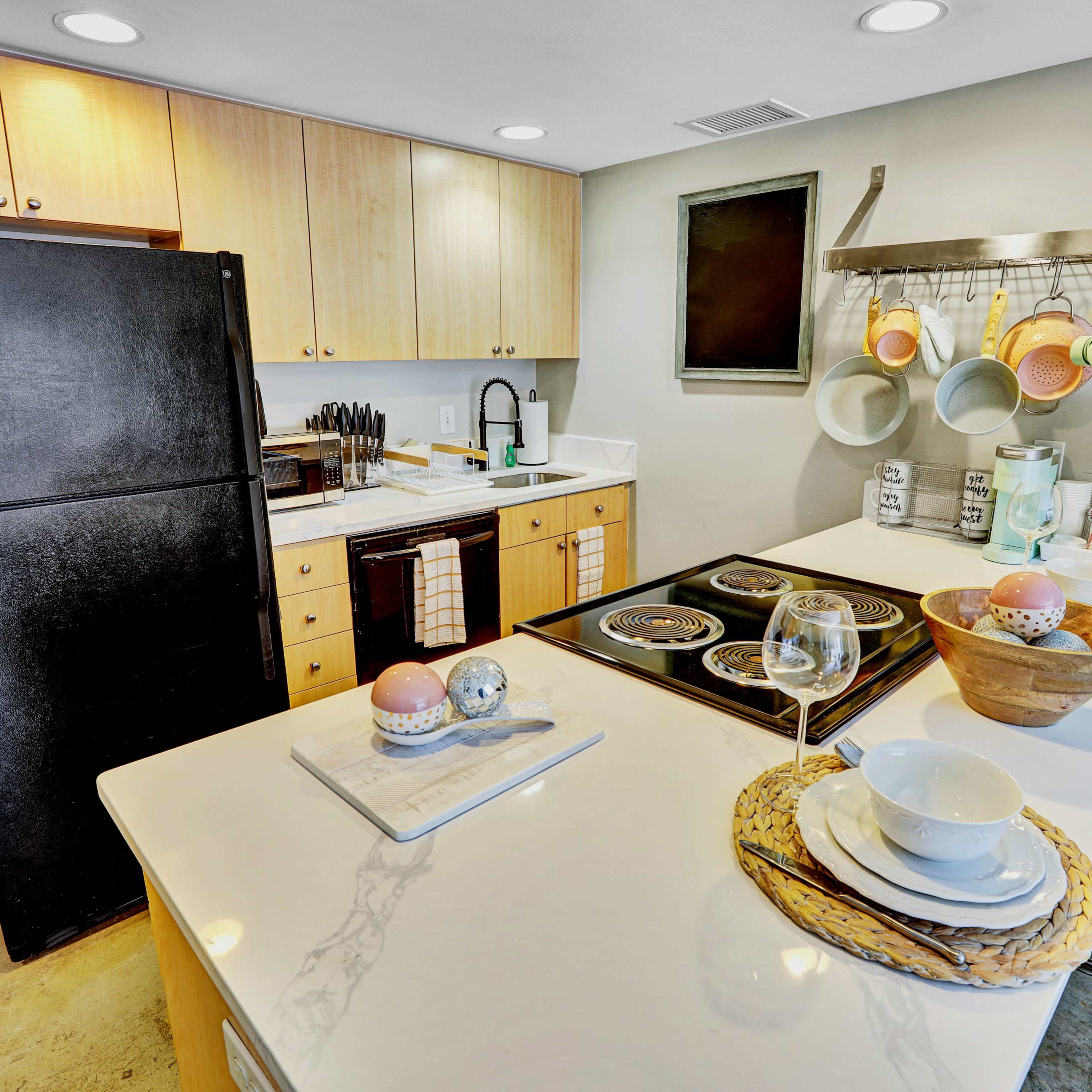 A modern kitchen with wooden cabinets, a black refrigerator, and an island featuring utensils and dishware.