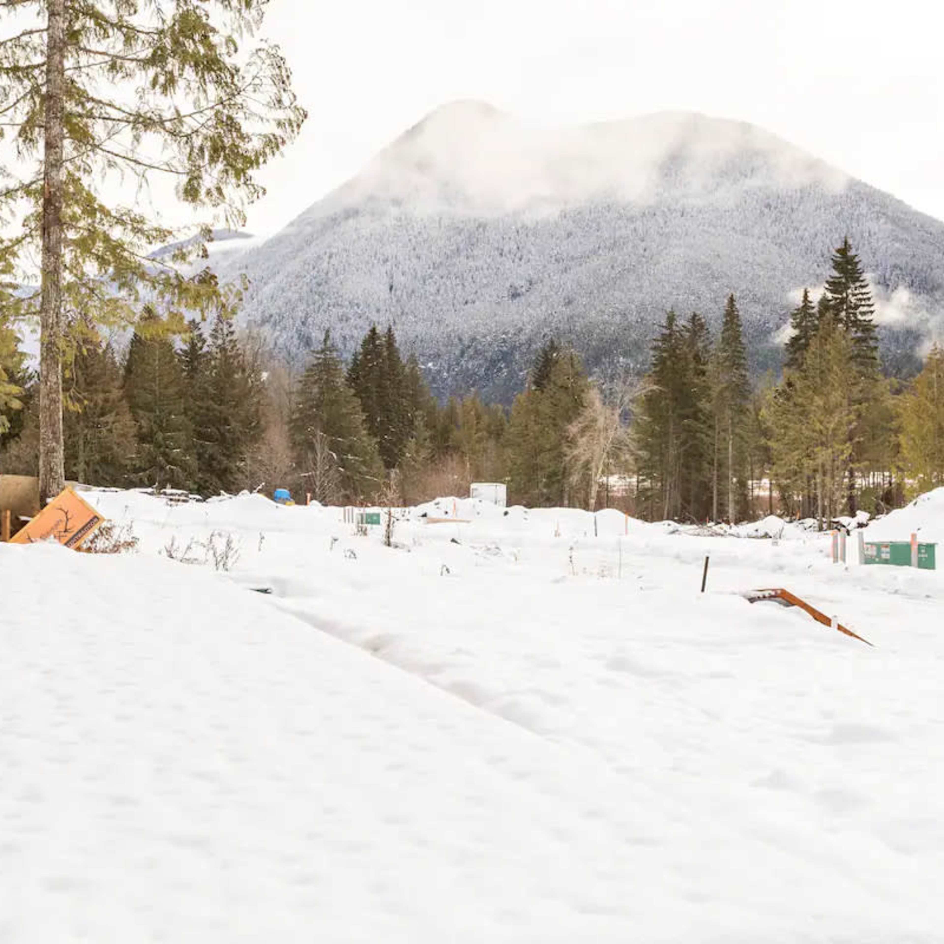 A modern building's wooden deck extends into a snowy landscape with mountains and trees in the background.