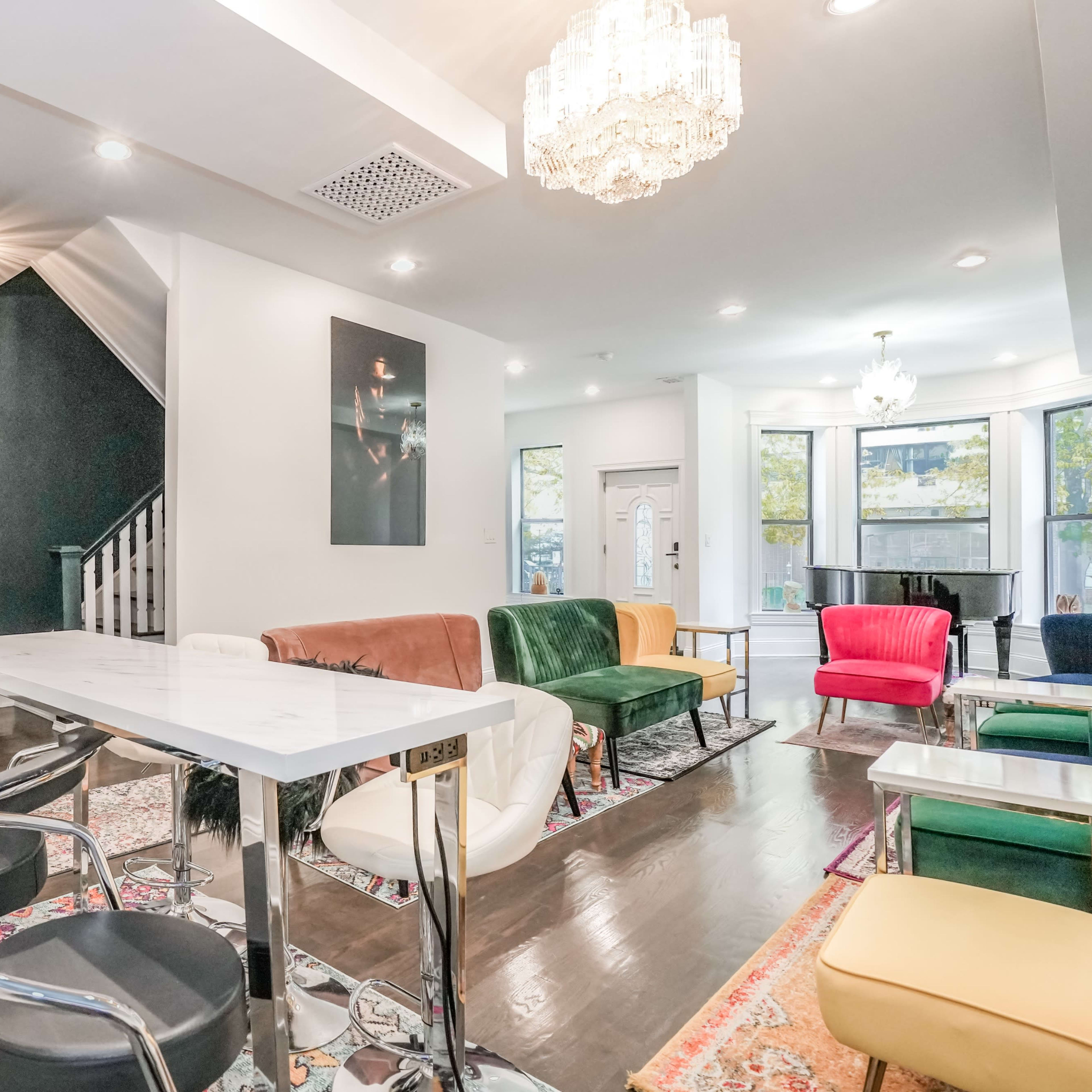 A modern living space featuring a dining table with high chairs, colorful sofas, and a staircase in the background.