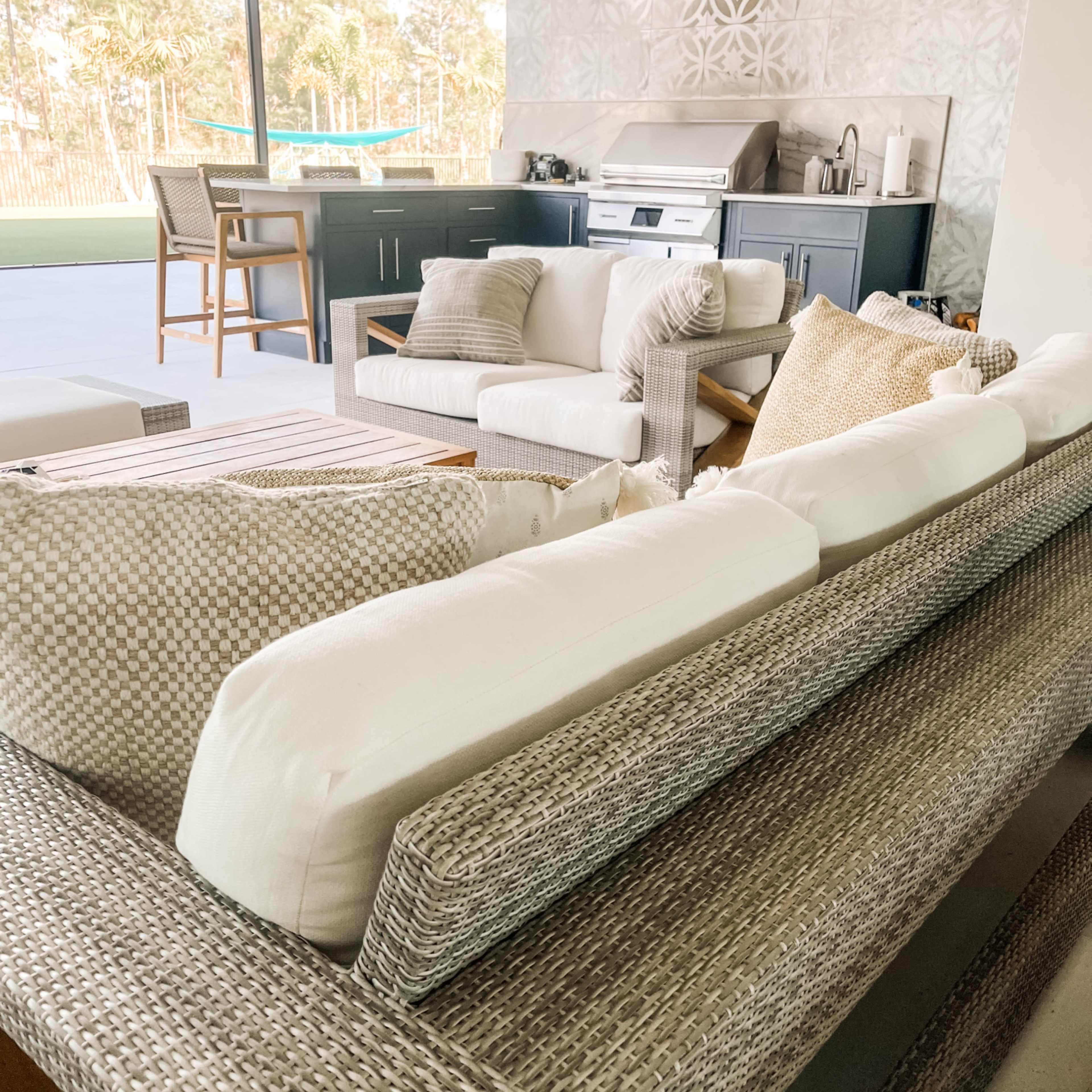 A modern outdoor living area features a woven sectional sofa and a sleek kitchen setup with a grill and counter space.