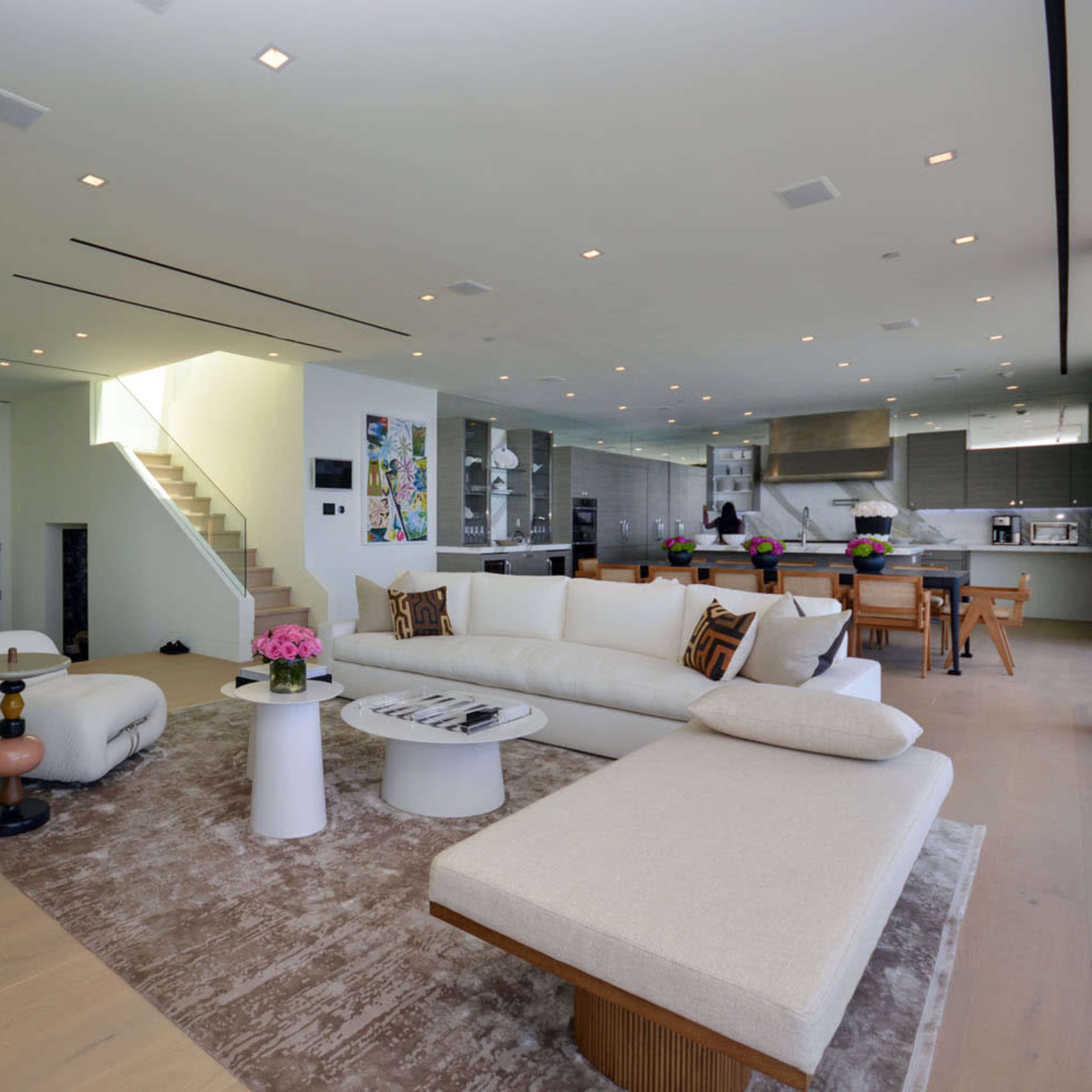A modern living room with a large sectional sofa, a coffee table, and an open kitchen area visible in the background.