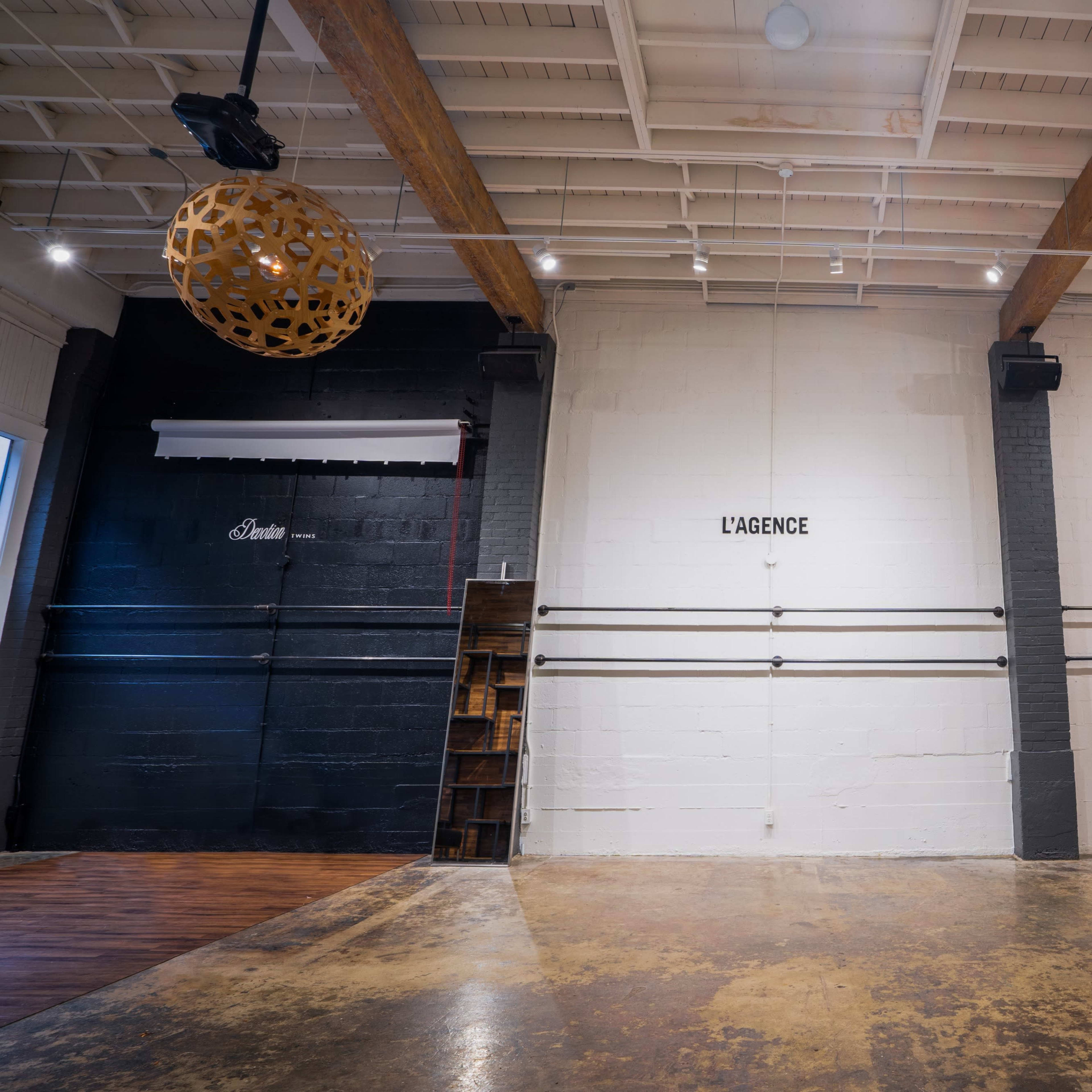 A spacious interior with two prominent walls featuring the words "L'AGENCE" and "KANGOL" painted on them, alongside decorative spherical light fixtures hanging from the ceiling.