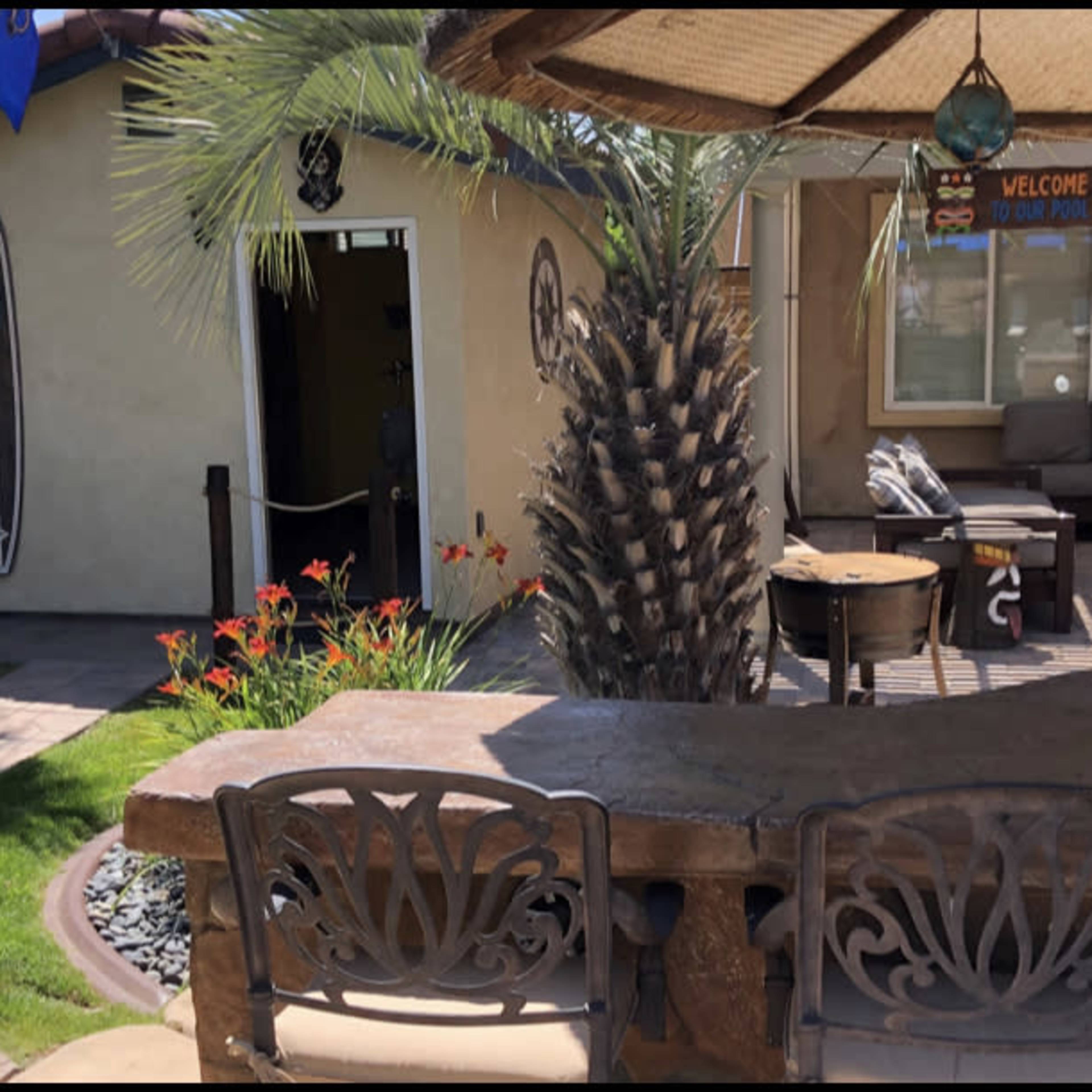 A backyard patio area with a stone bar, seating, palm trees, and a door leading into the house.