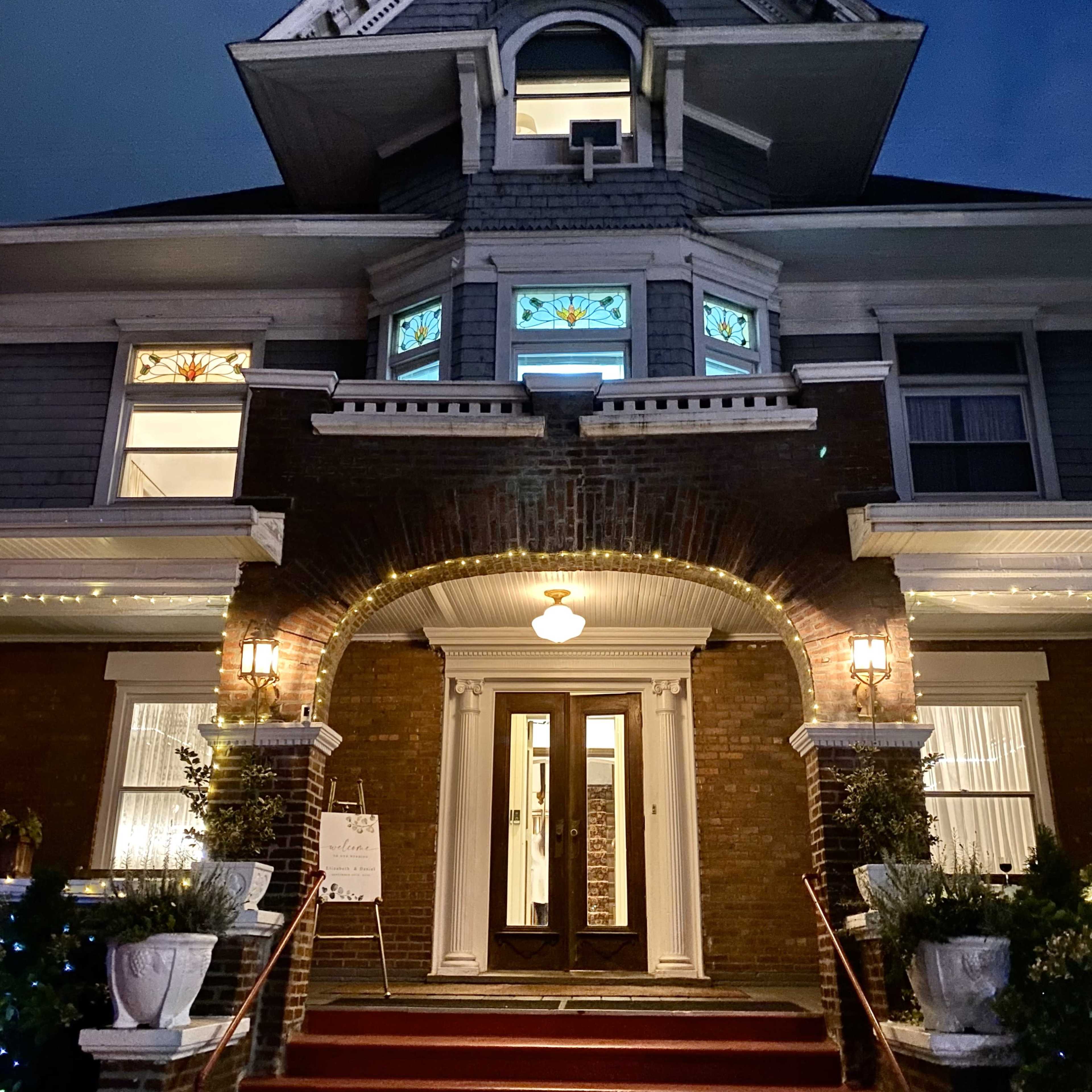 A large, illuminated historic house with decorative stained glass windows and a welcoming entrance.