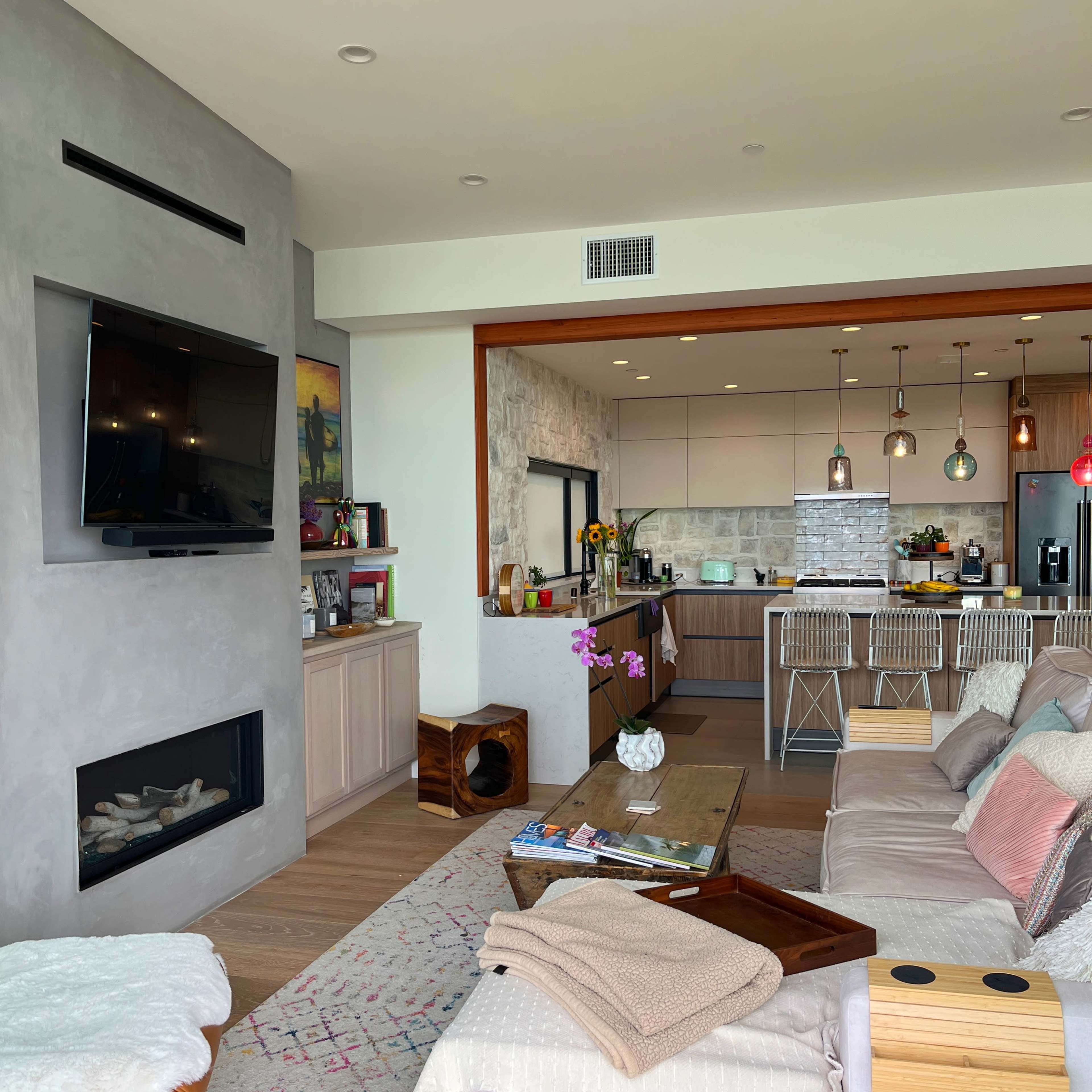 A modern living room with a fireplace and a view of an open kitchen, featuring a mix of light wood and gray decor.
