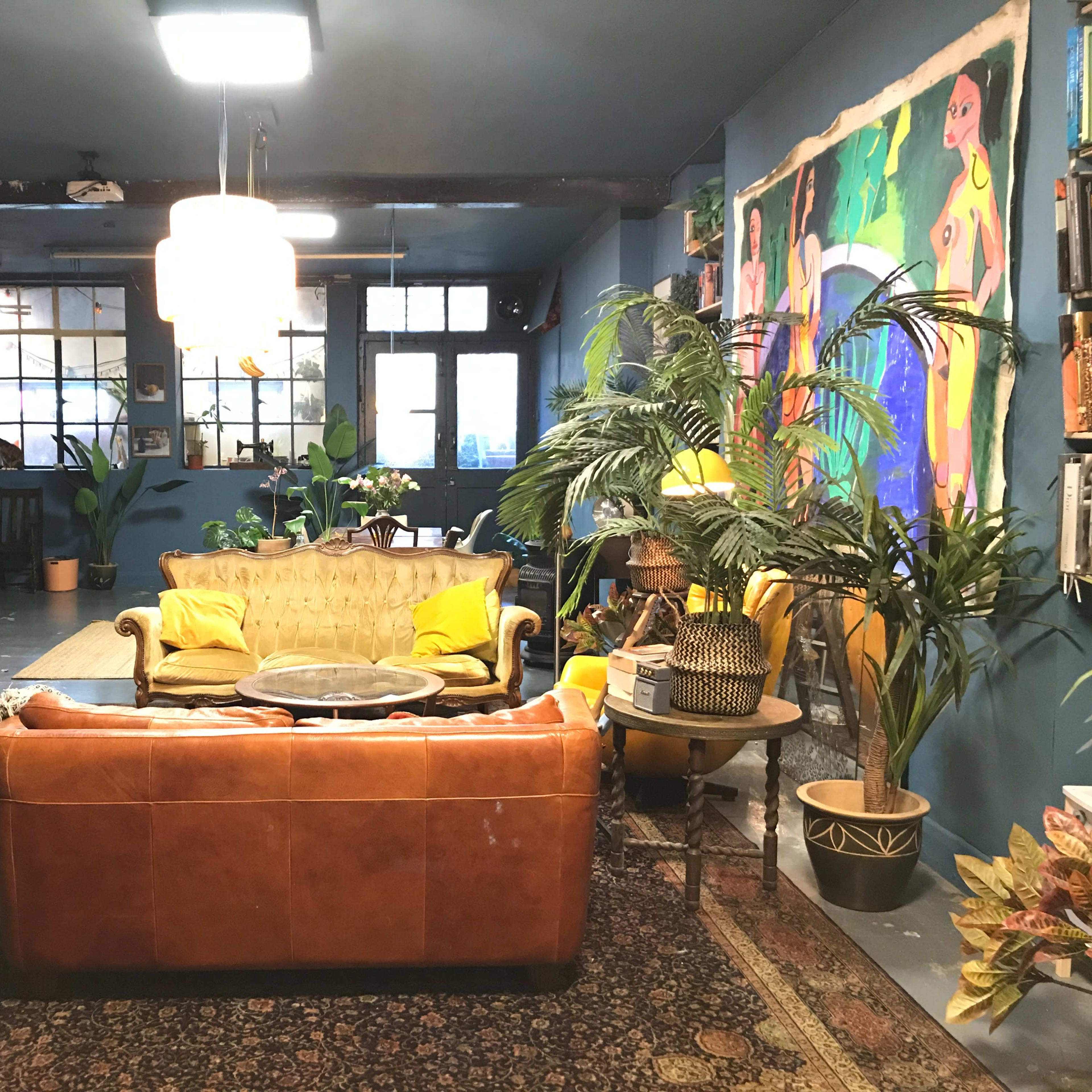 A spacious room decorated with blue walls, featuring a leather sofa, a round coffee table, plants, and colorful artwork.
