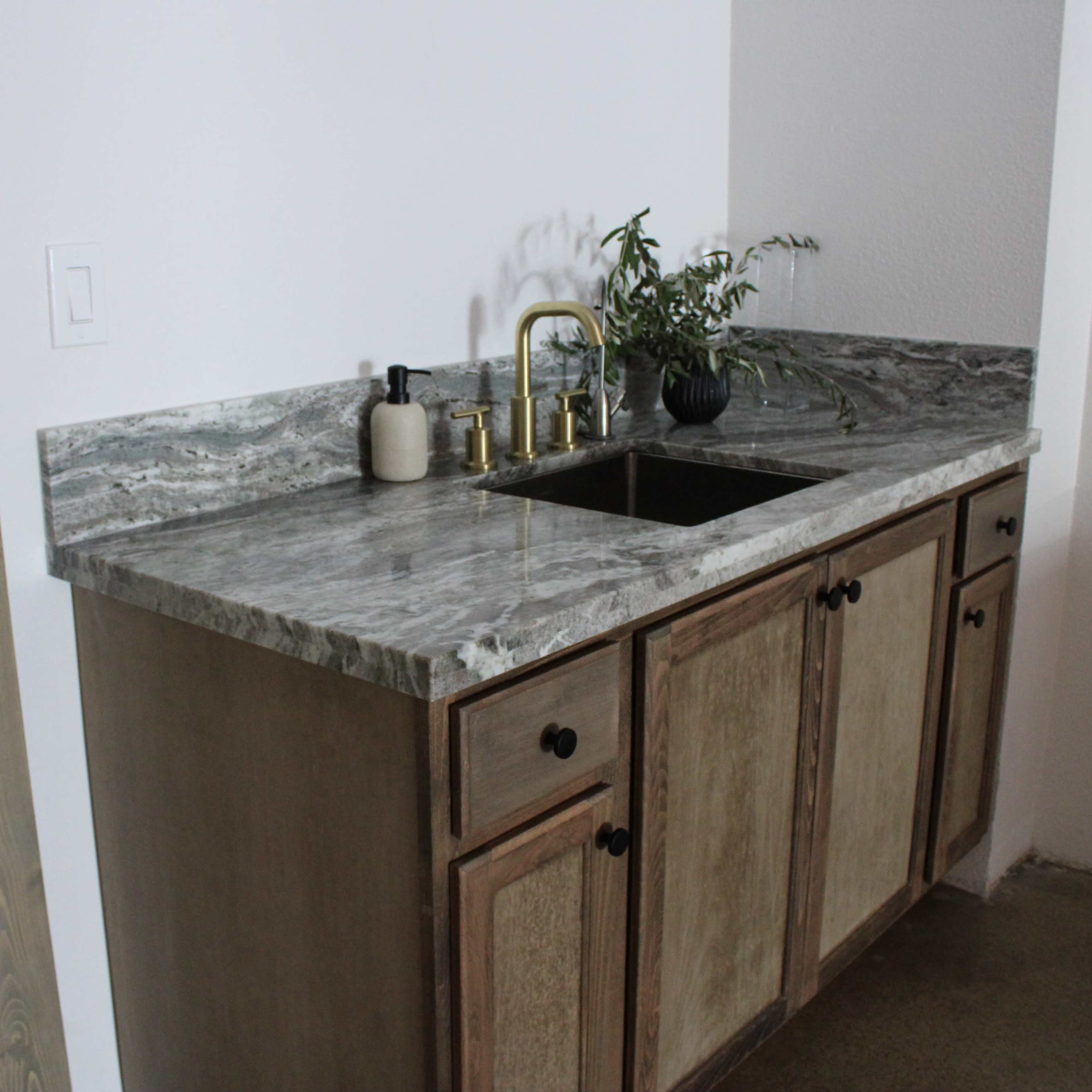 A modern kitchen countertop made of patterned stone with a sink and decorative items on top, adjacent to a wooden cabinet.