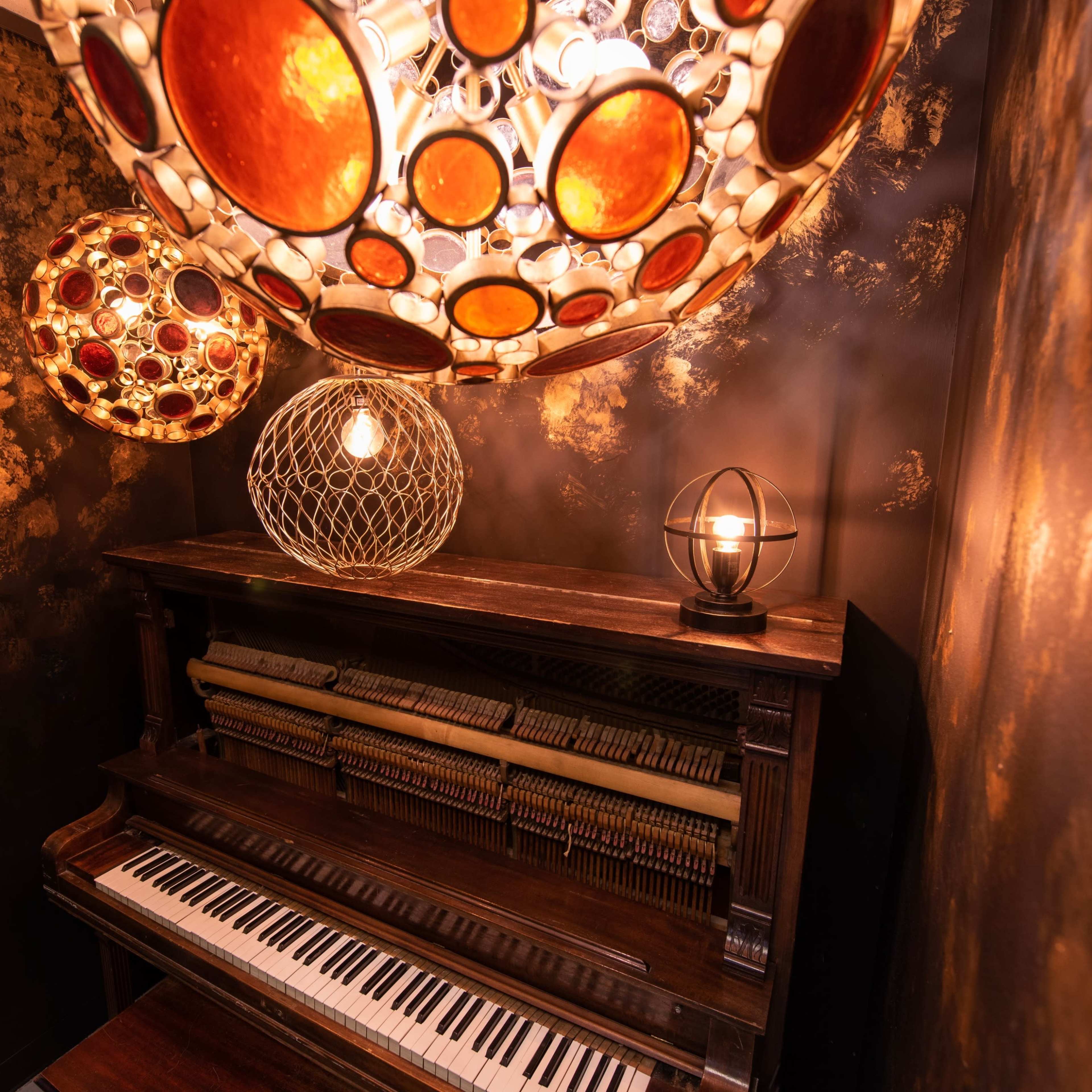 A wooden piano is positioned against a dark wall adorned with decorative lighting fixtures.