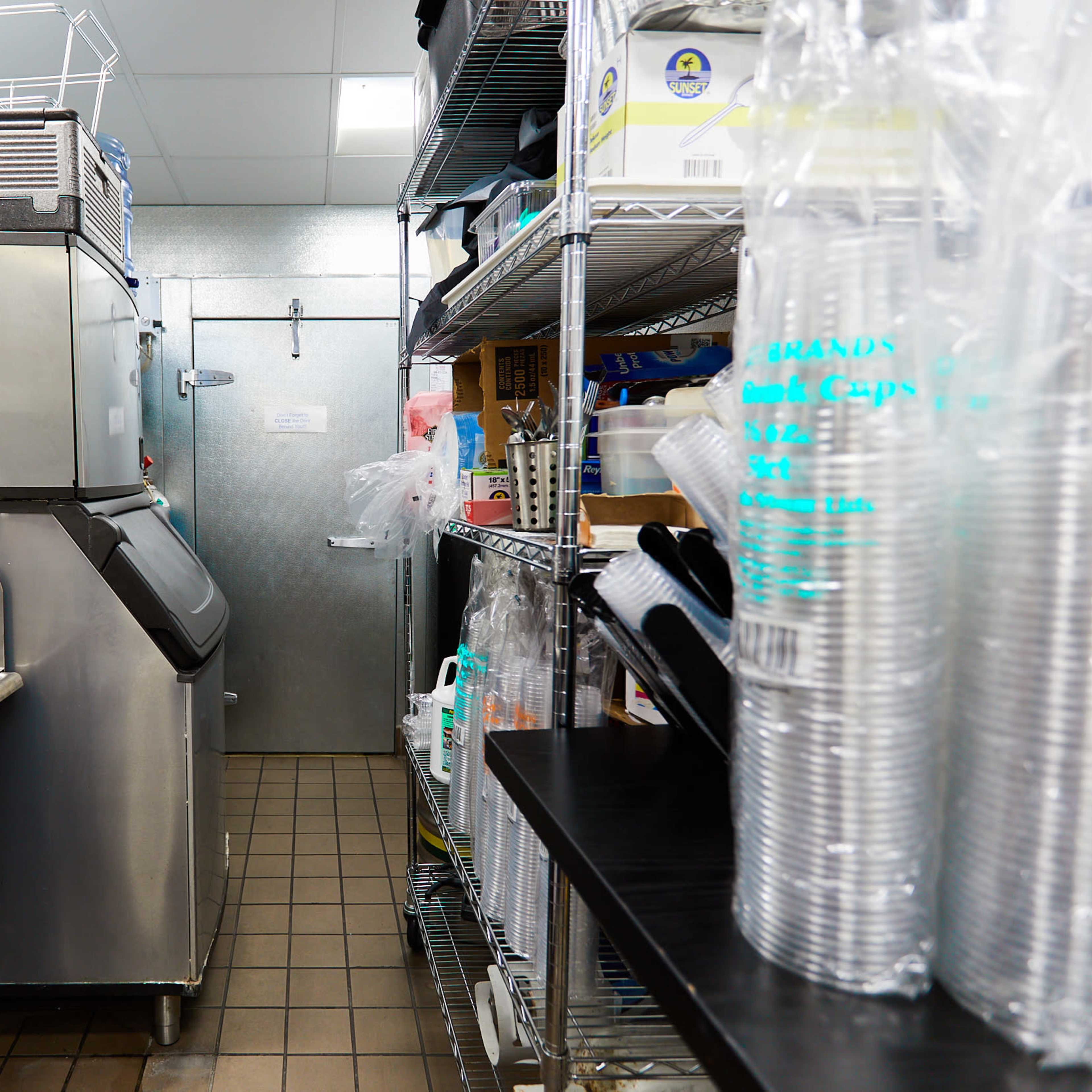 A commercial kitchen area featuring an ice machine, a stainless steel sink, shelving units, and a door leading to another space.